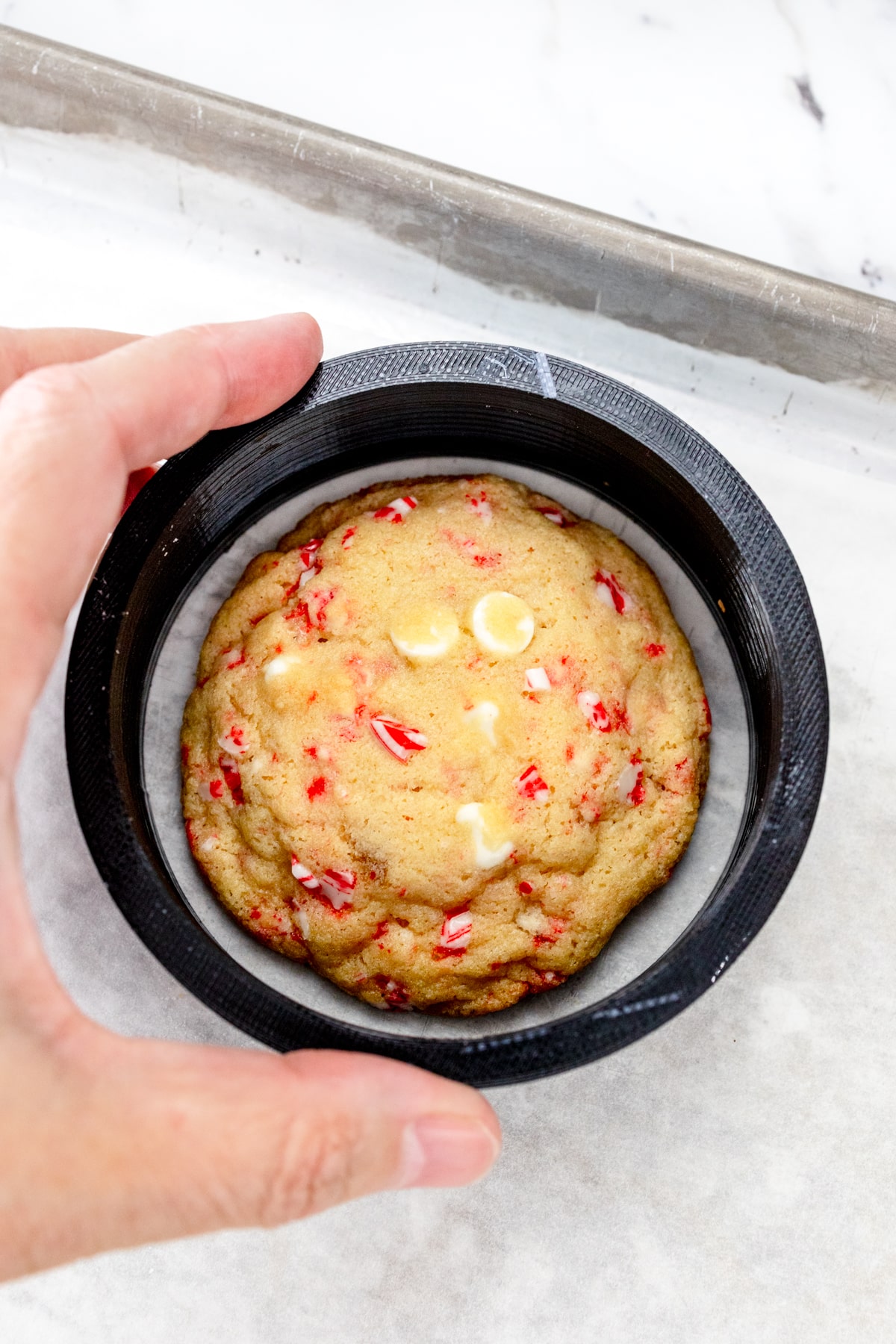Top view of a freshly baked White Chocolate Peppermint Cookie with a large cookie cutter being placed around it to make it into a perfect circle.