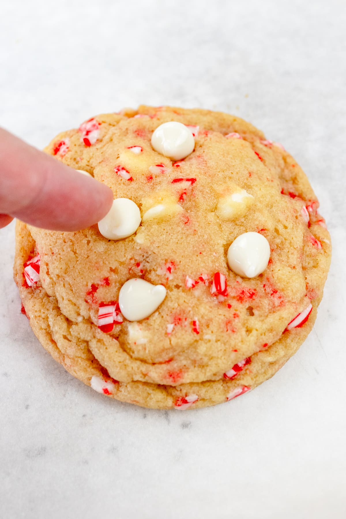 Top view of a freshly baked White Chocolate Peppermint Cookie with fingers pressing more white chocolate chips into the top.