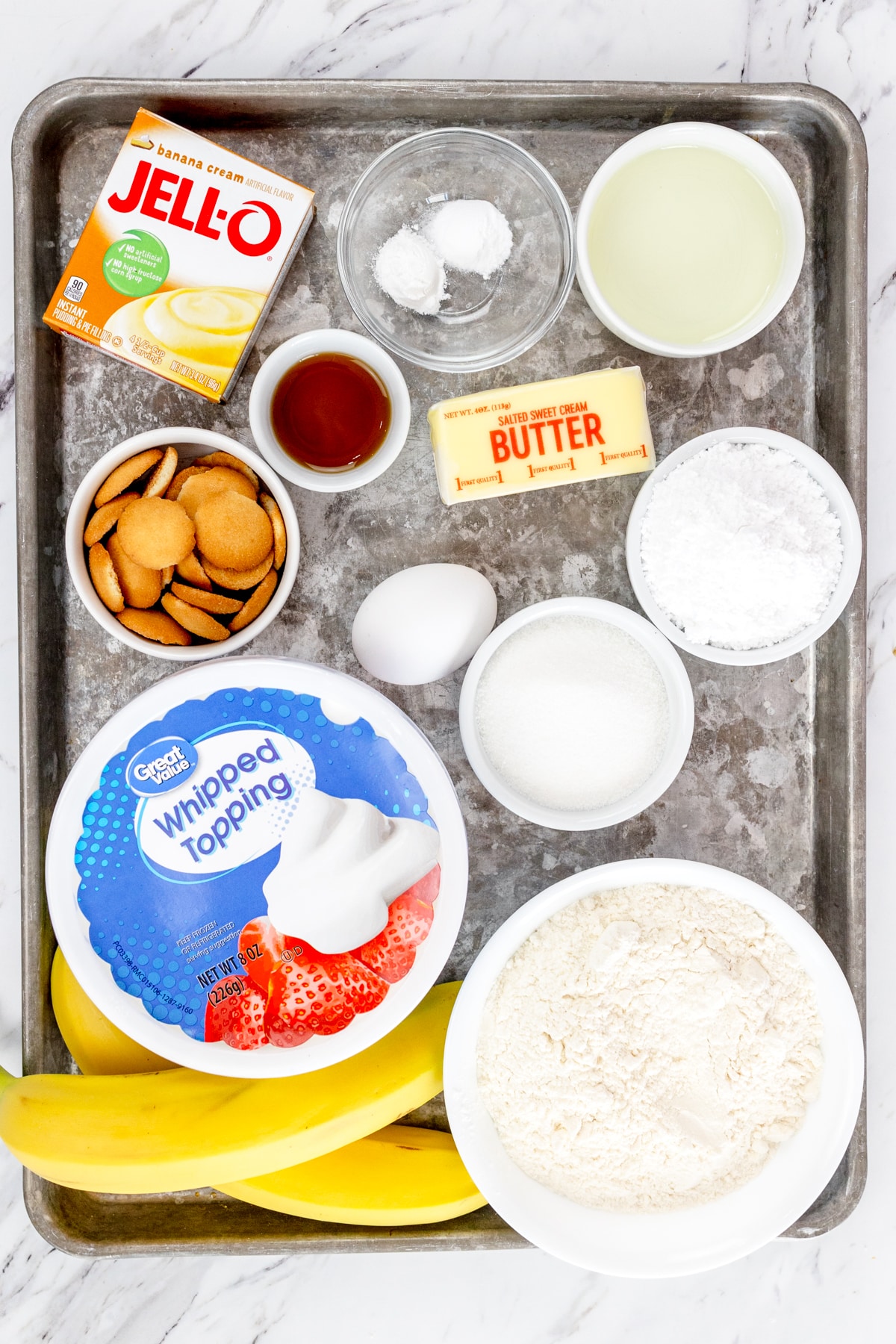 Top view of ingredients needed to make Banana Cream Pie Cookies in small bowls on a baking tray.