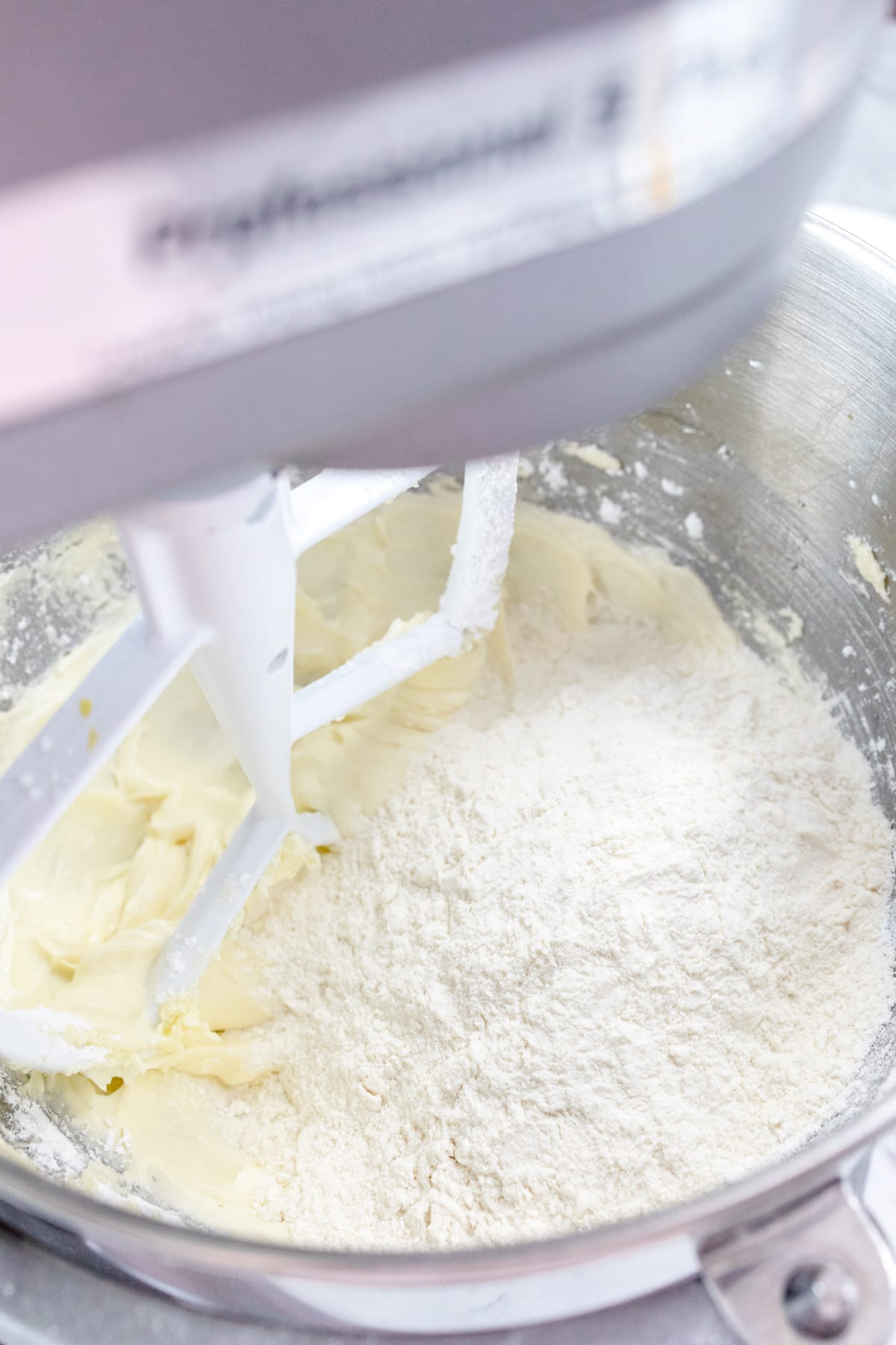 Close up of the bowl of a stand mixer with a creamed mixture in it with powdered sugar on top.