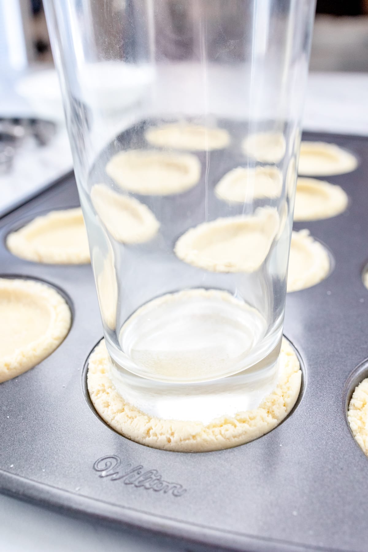 Close up of the bottom of a glass that has been dipped in sugar, pressing the cookie dough down flat into the muffin top pan.