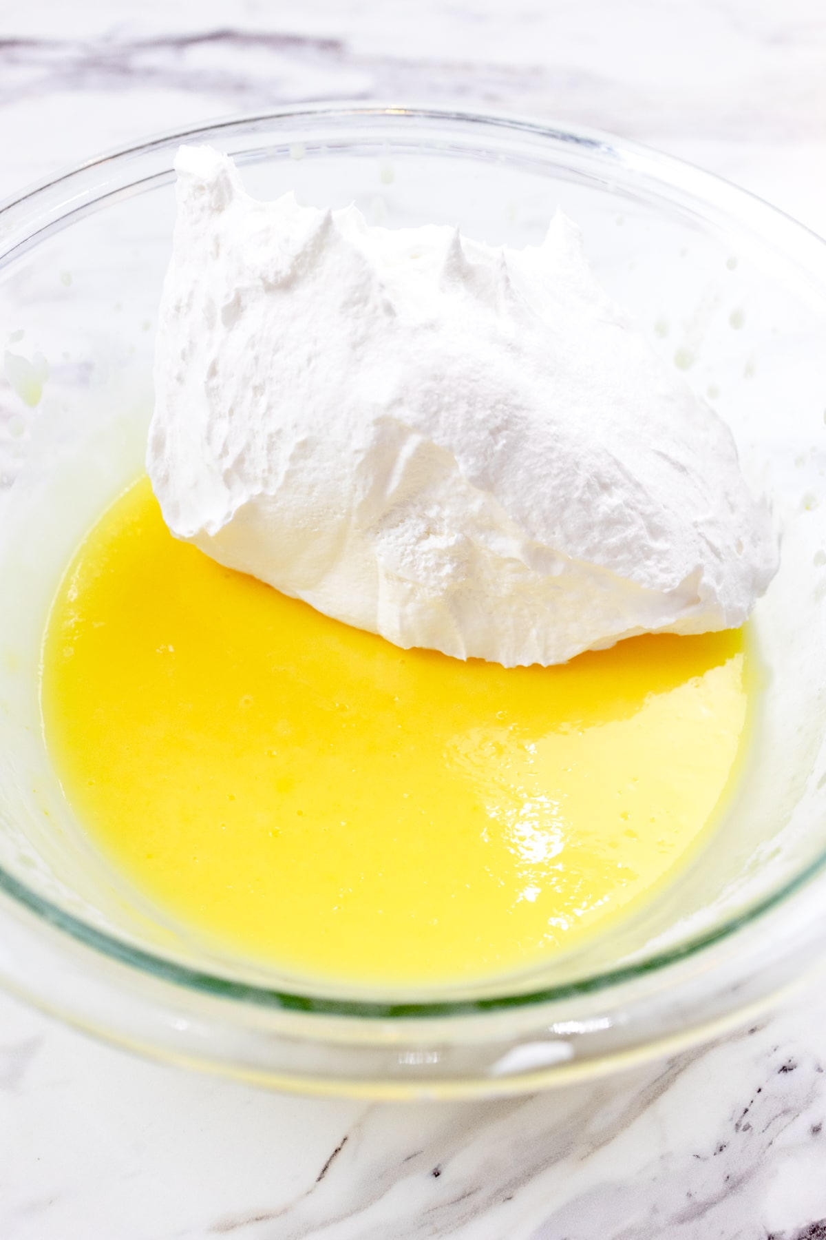 Close up of a glass mixing bowl which contains cool whip and the vanilla pudding.