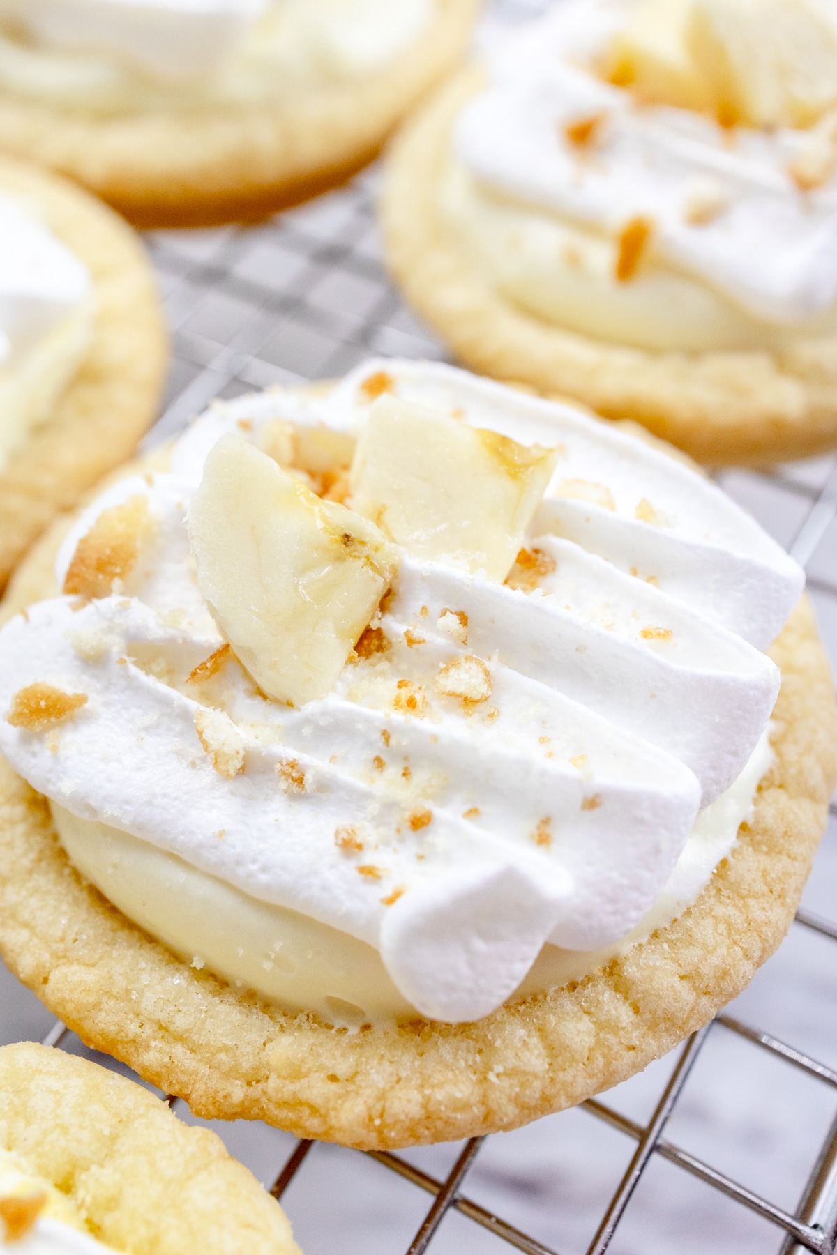 Close up of finished Banana Cream Pie Cookies on a wire rack garnished with banana slices and sprinkled with mini nilla wafer crumbles.