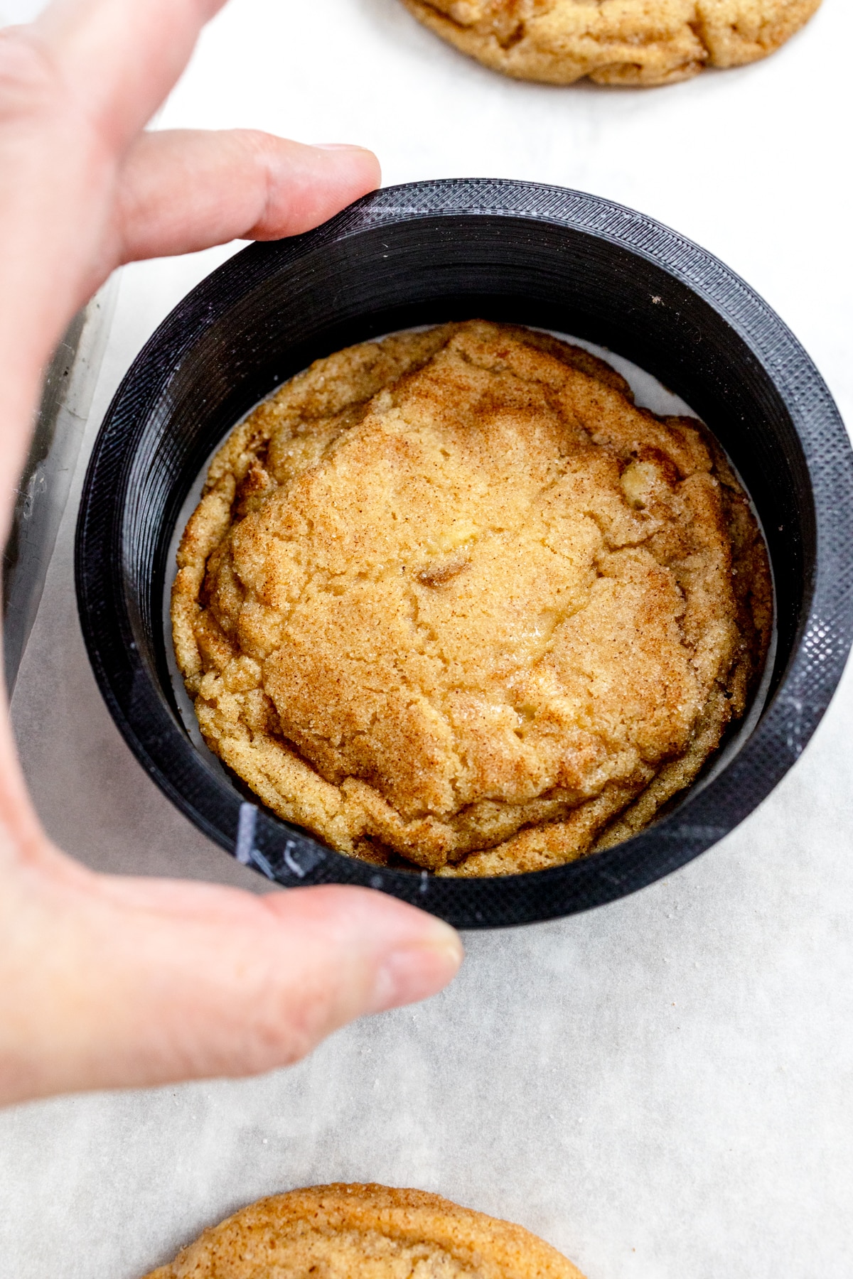 Top view of a freshly baked Caramel Apple Cookie with a large cookie cutter being placed around it to make it into a perfect circle.