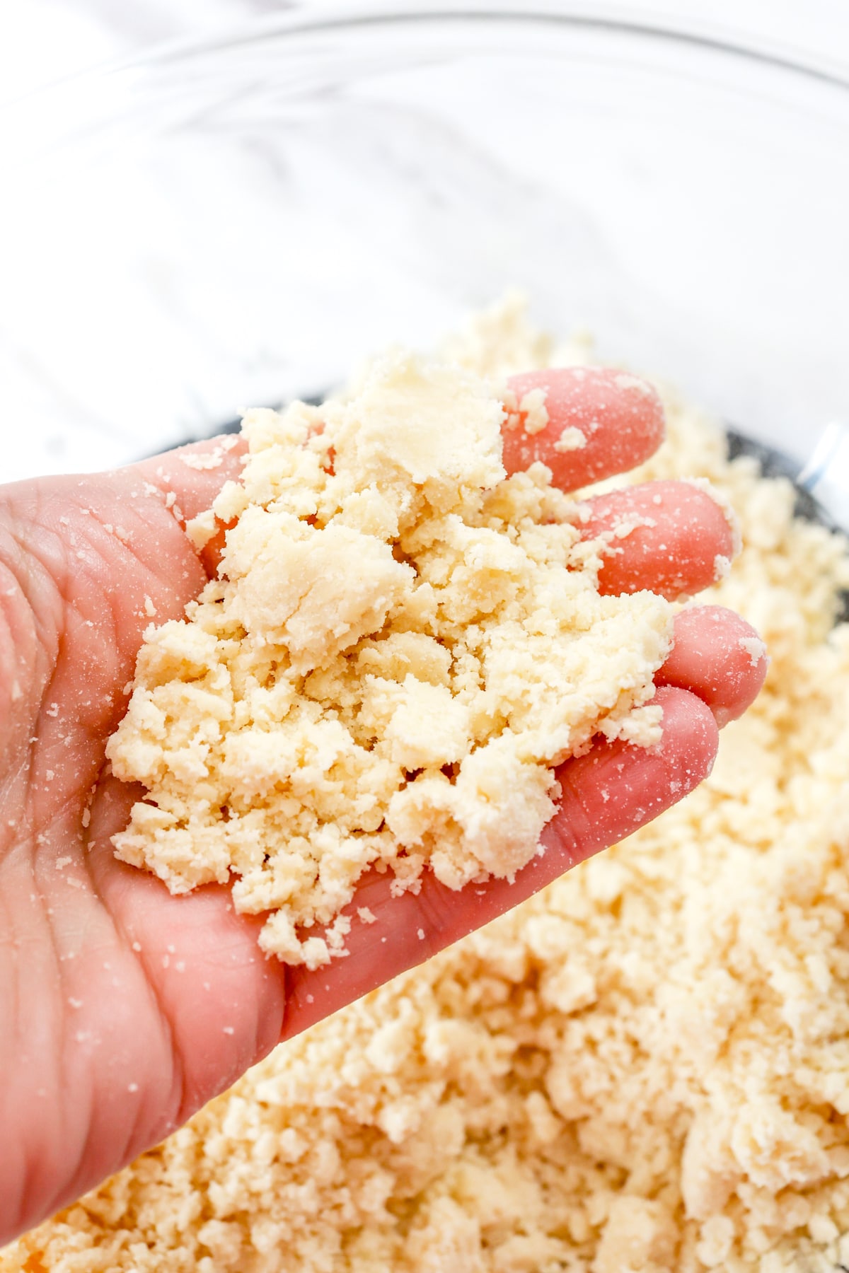Close up of a hand holding blended butter and all-purpose flour above a mixing bowl.