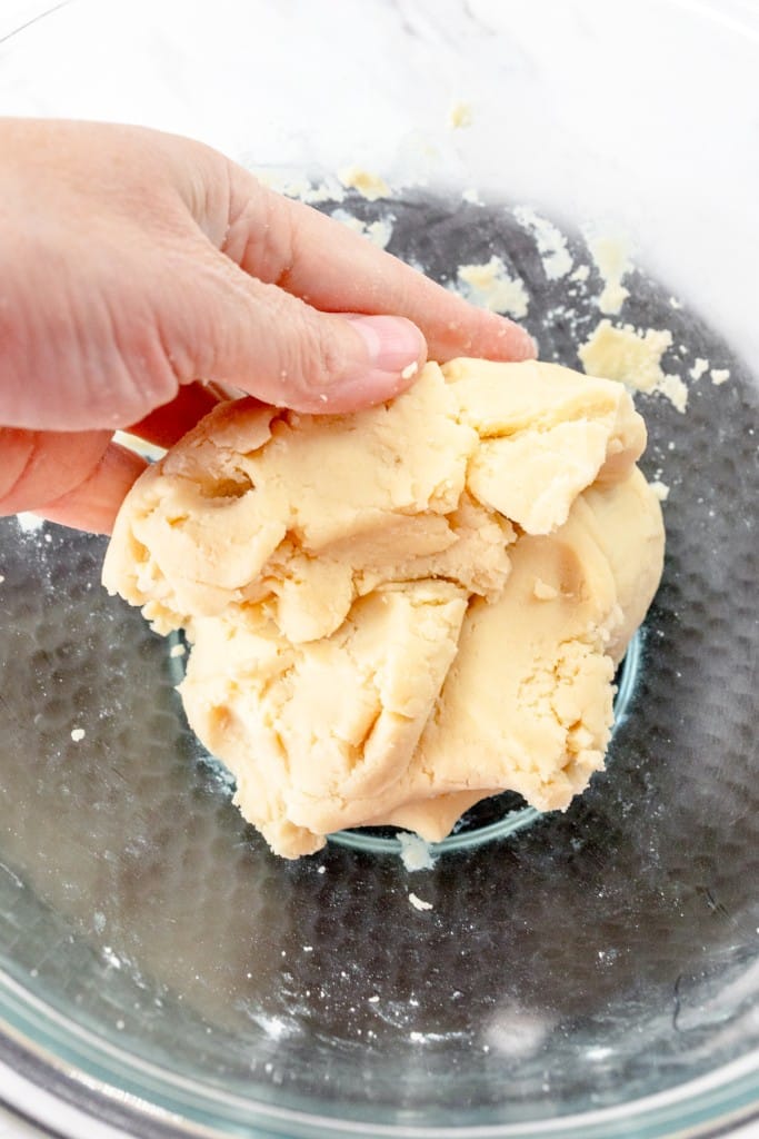 Close up of a hand kneading the dough together in a mixing bowl.