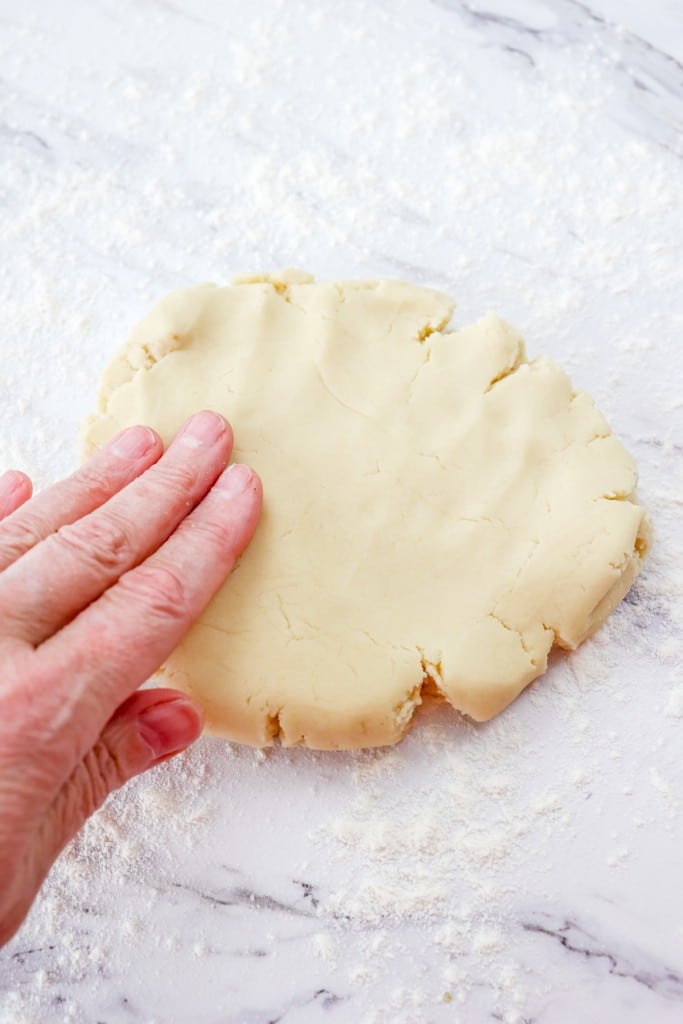 Close up of a hand pressing out cookie dough on a counter sprinkled with a light dusting of flour.