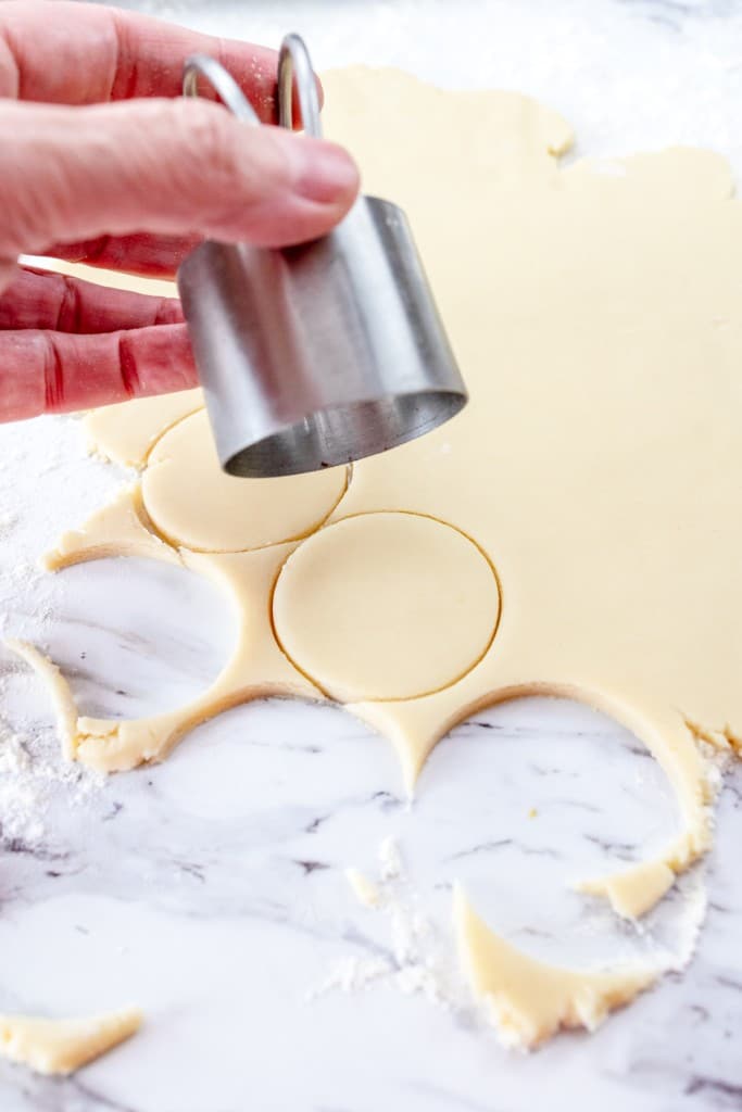 Close up of a hand holding a circle cookie cutter, cutting out 2-inch circles from the rolled out dough.