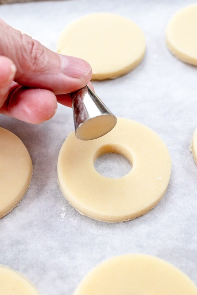 Close up of a hand holding a piping tip to cut out holes from the center of half of the cookies.