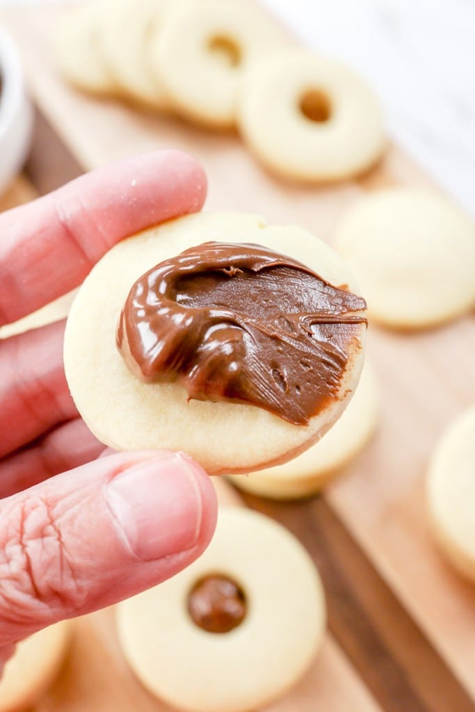 Close up of a hand holding a cookie with a dollop of chocolate spread on it.