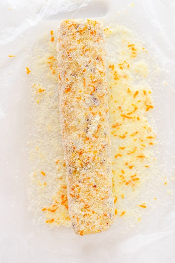 Top view of a log of cookie dough being coated in coarse sugar and orange zest.