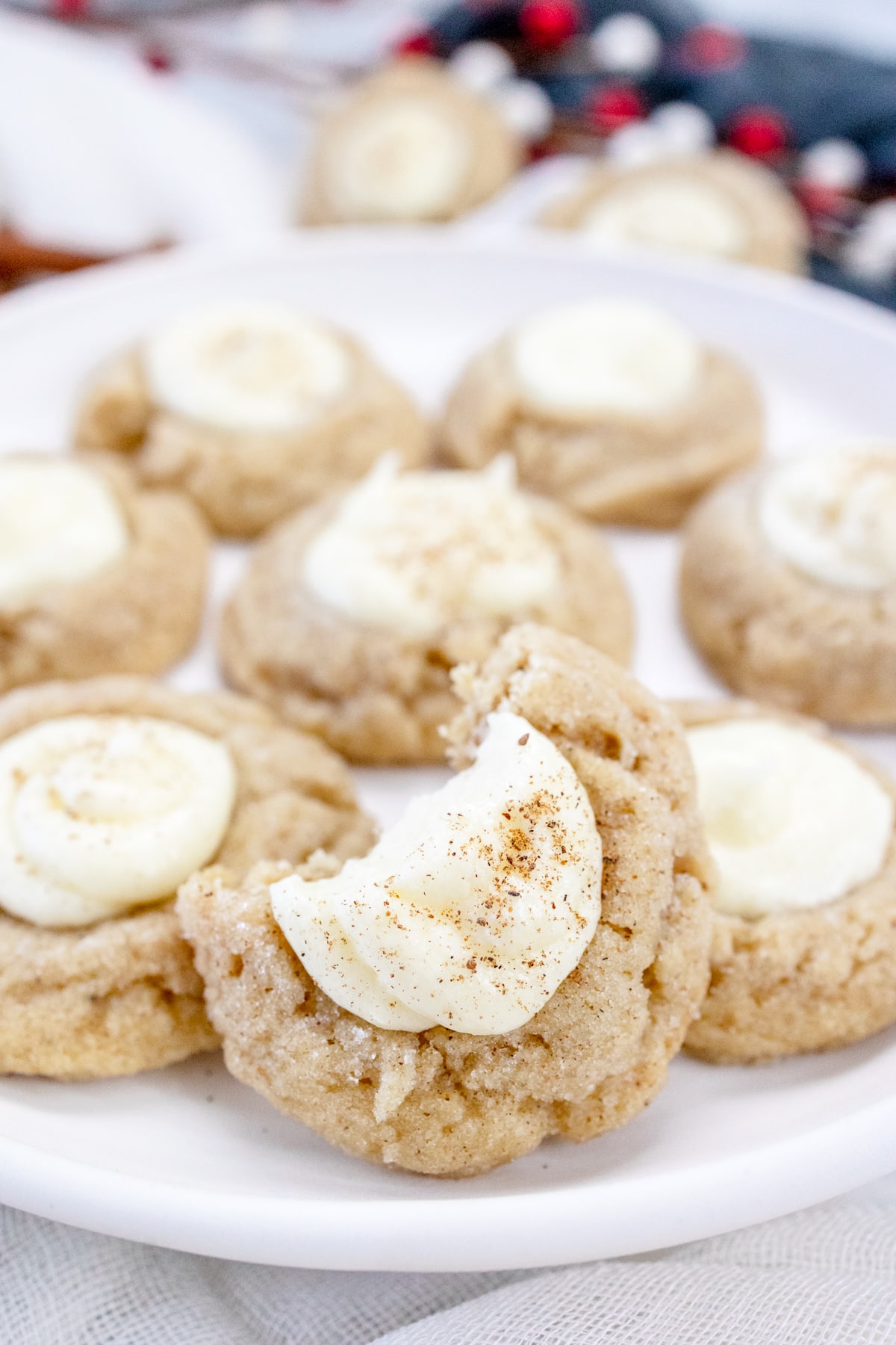 Close up of Eggnog Thumbprint Cookies on a white plate. The foremost cookie has had a bite taken out of it.