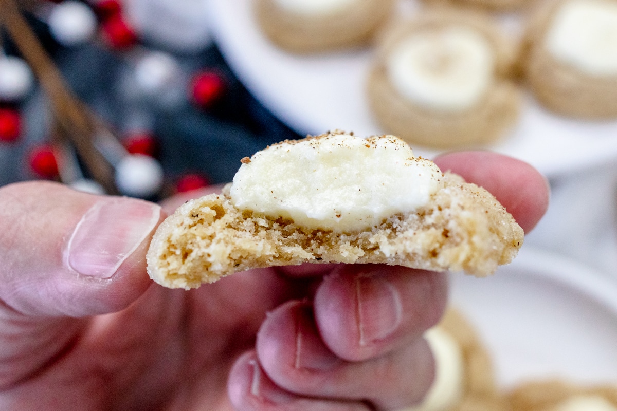 Close up view of a hand holding an Eggnog Thumbprint Cookie that's been sliced in half to reveal the middle.