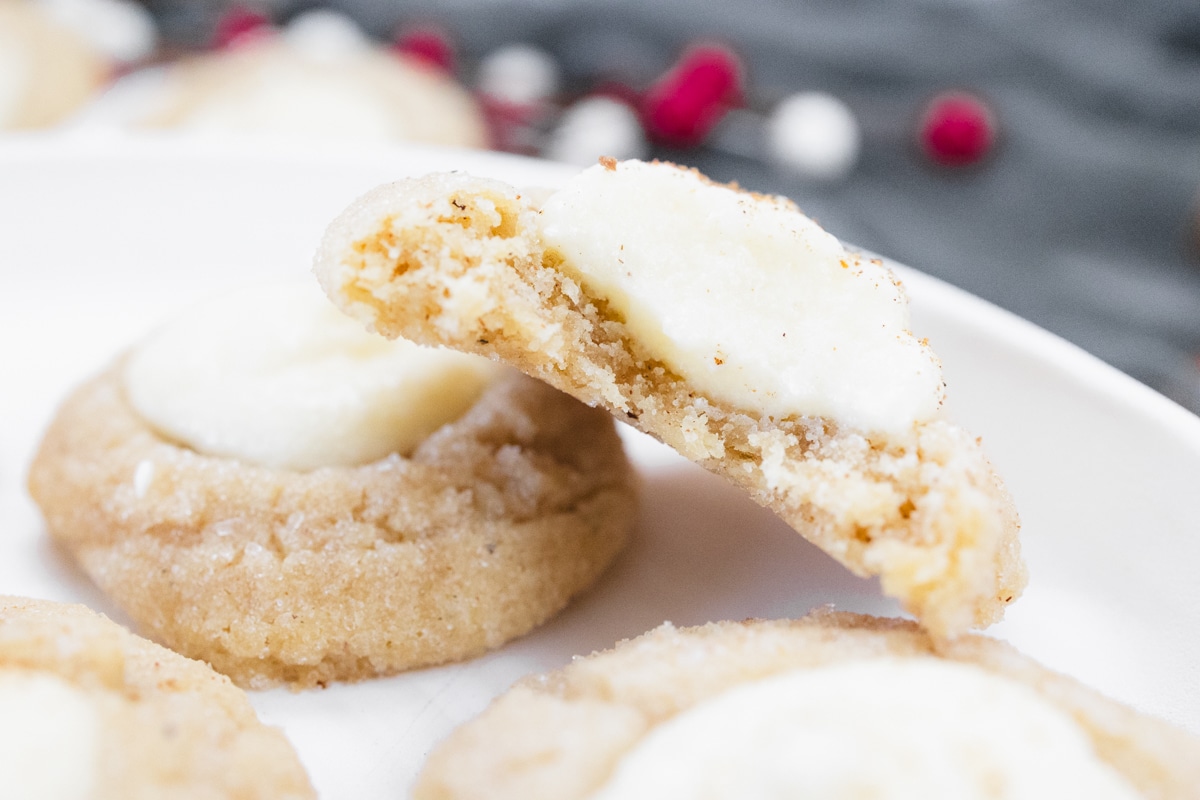 Close up view of Eggnog Thumbprint Cookie sliced in half to reveal the middle, balanced on top of another Eggnog Thumbprint Cookie.