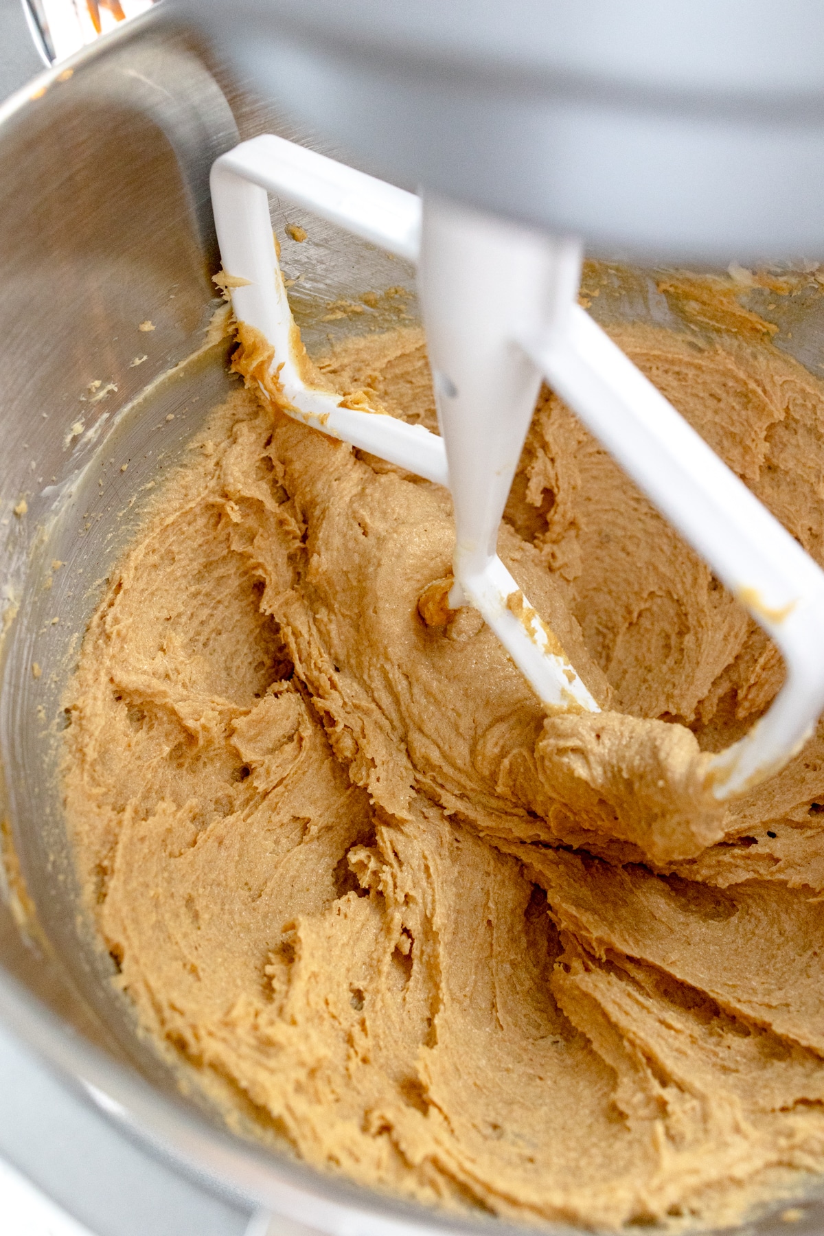 Close up of the bowl of a stand mixer with butter and brown sugar being creamed together with a paddle attachment.