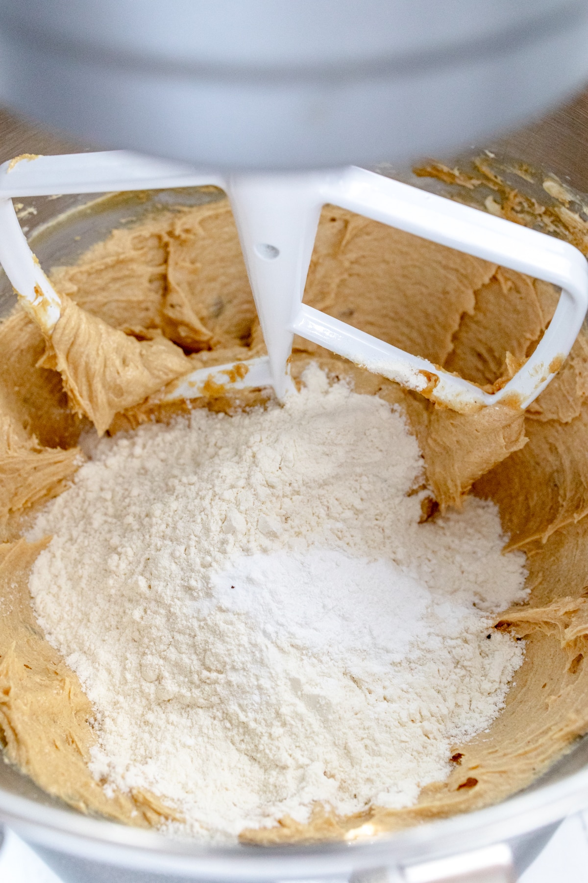 Close up of the bowl of a stand mixer with dry and wet ingredients ready to be mixed together with a paddle attachment.