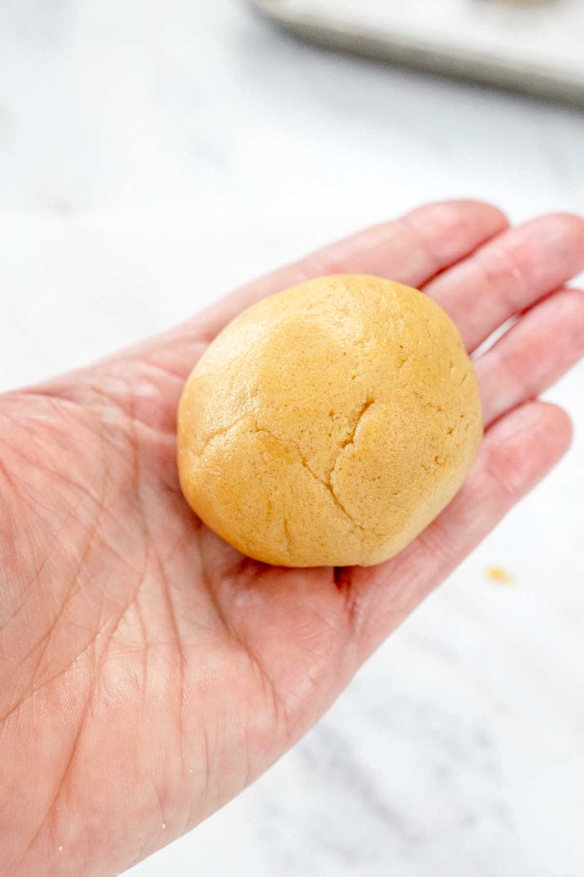 Close up of a flattened cookie dough ball with marshmallow fluff in the center, being sealed and rolled into a round ball again.