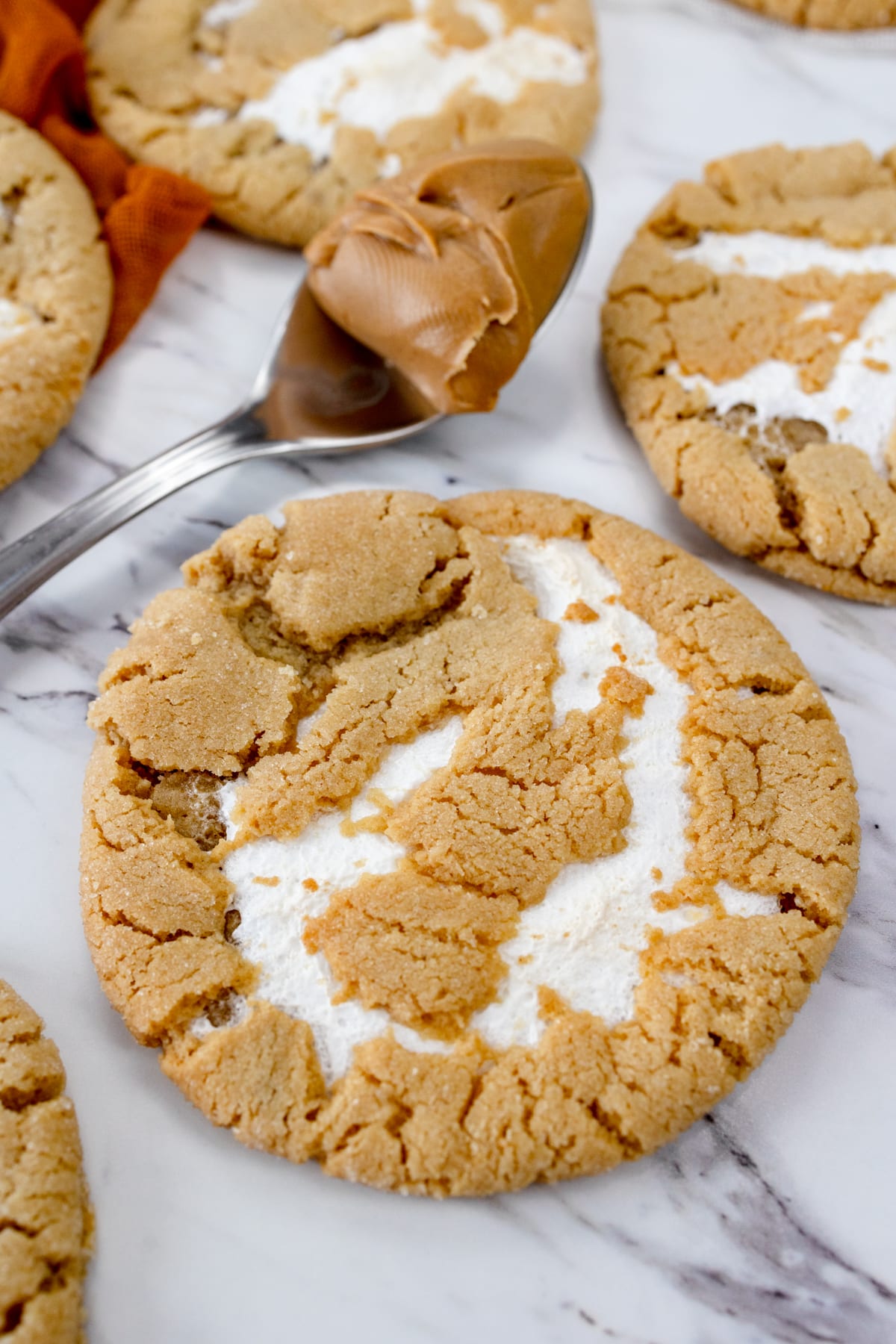 Top view of Fluffernutter Cookies next to a teaspoon of peanut butter on a decorated table.