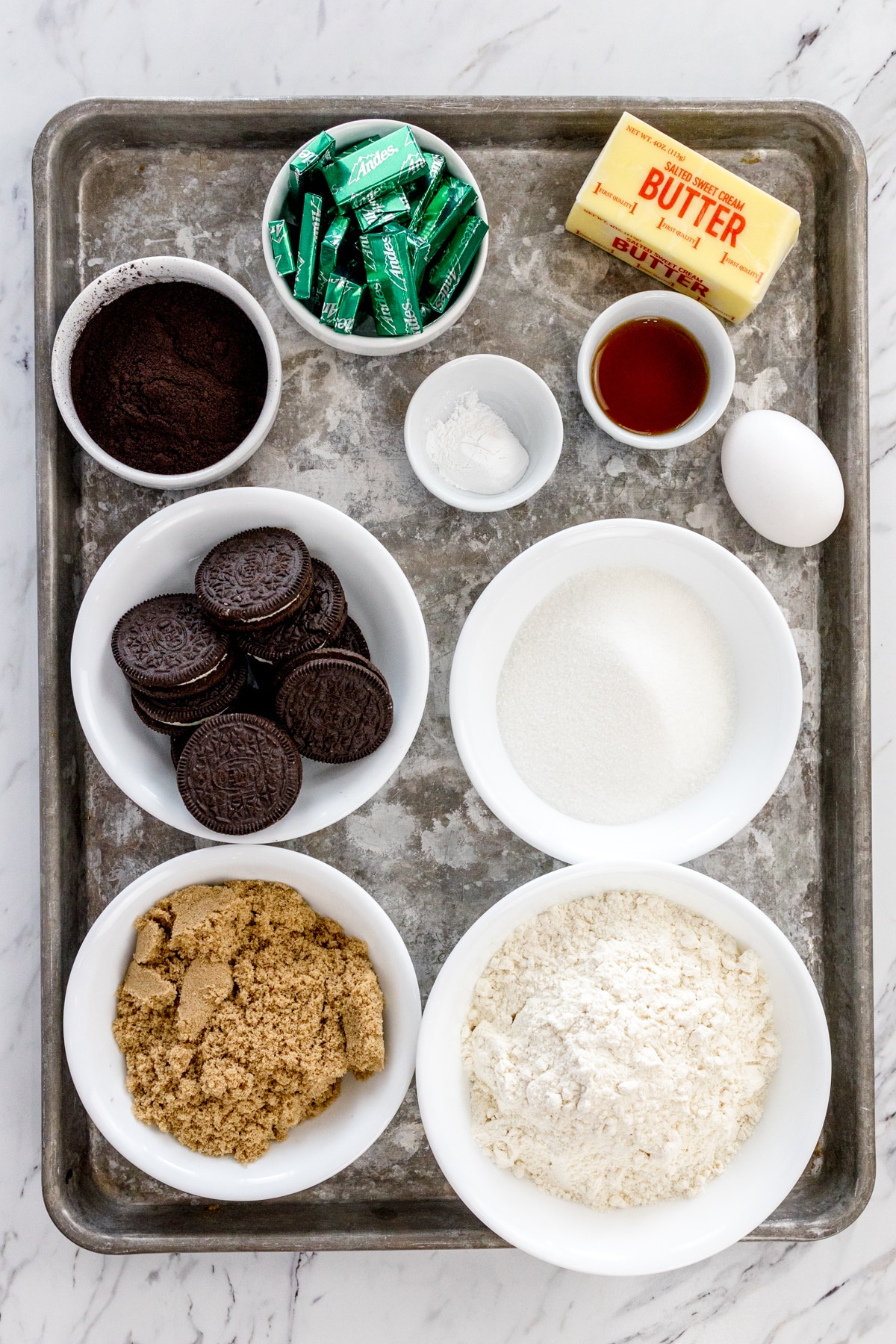 Top view of ingredients needed to make Frosted Mint Oreo Cookies in small bowls on a baking tray.