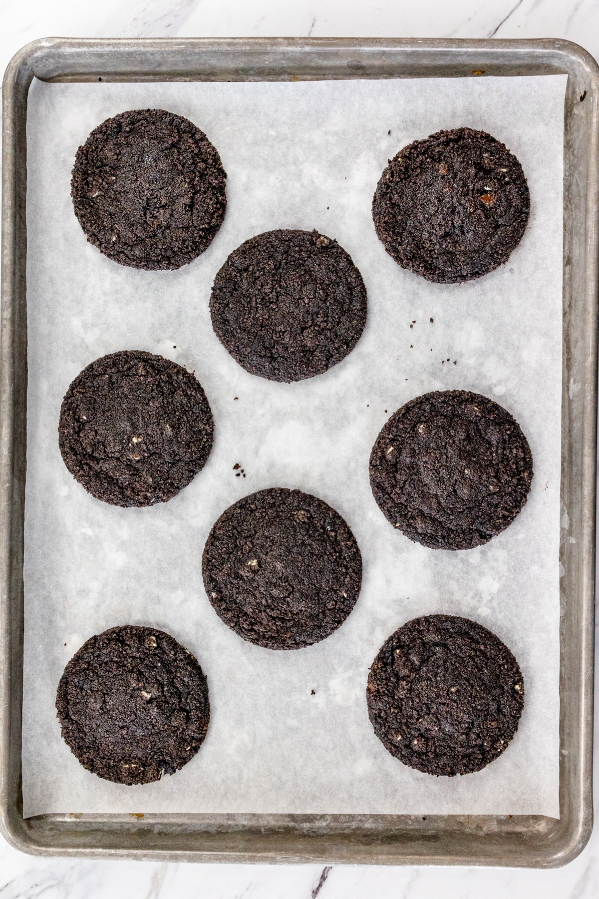 Top view of baking tray lined with parchment paper with freshly baked Frosted Mint Oreo Cookies on it.