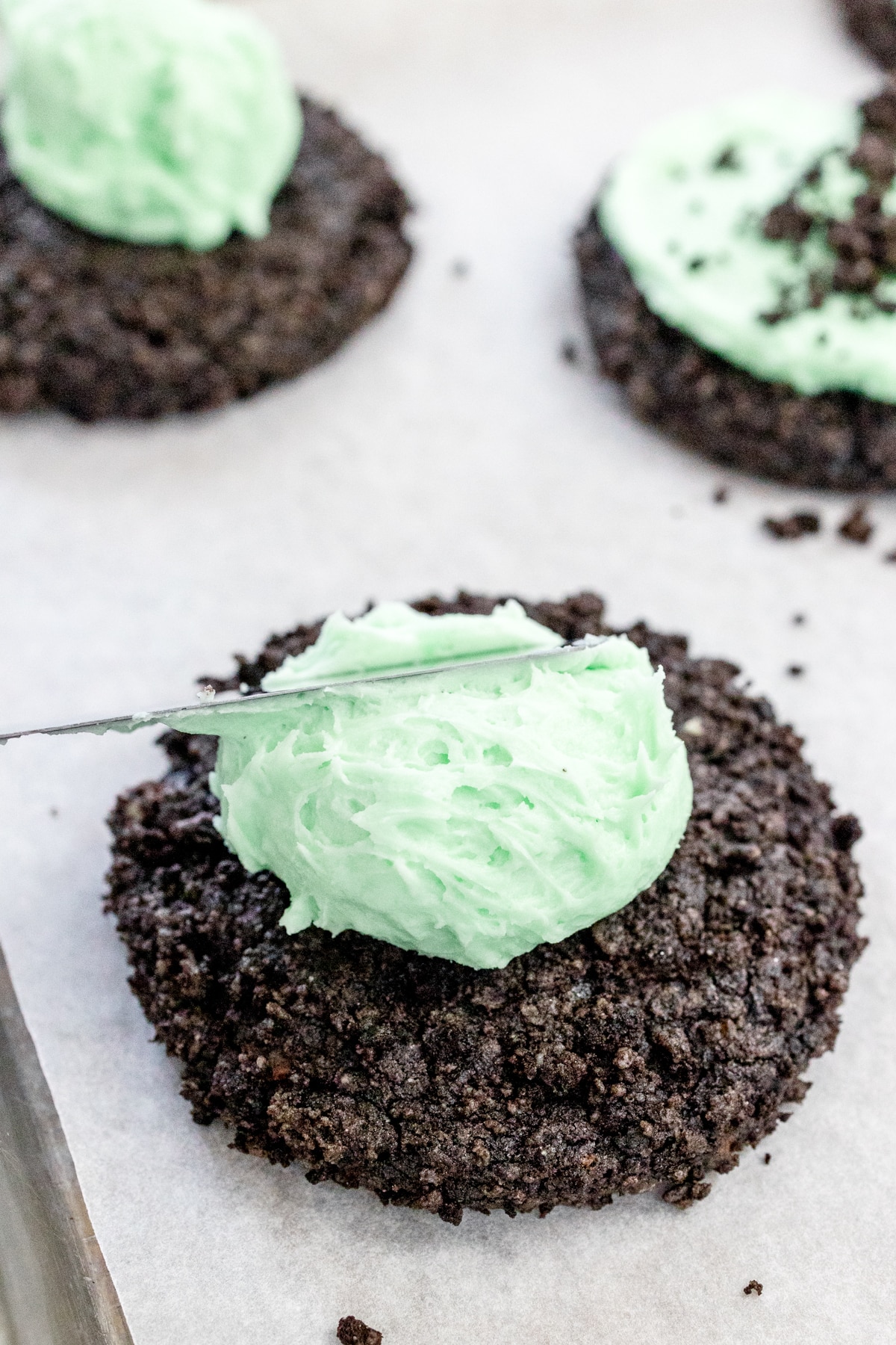 Close up of a butterknife spreading mint frosting onto a mint oreo cookie.