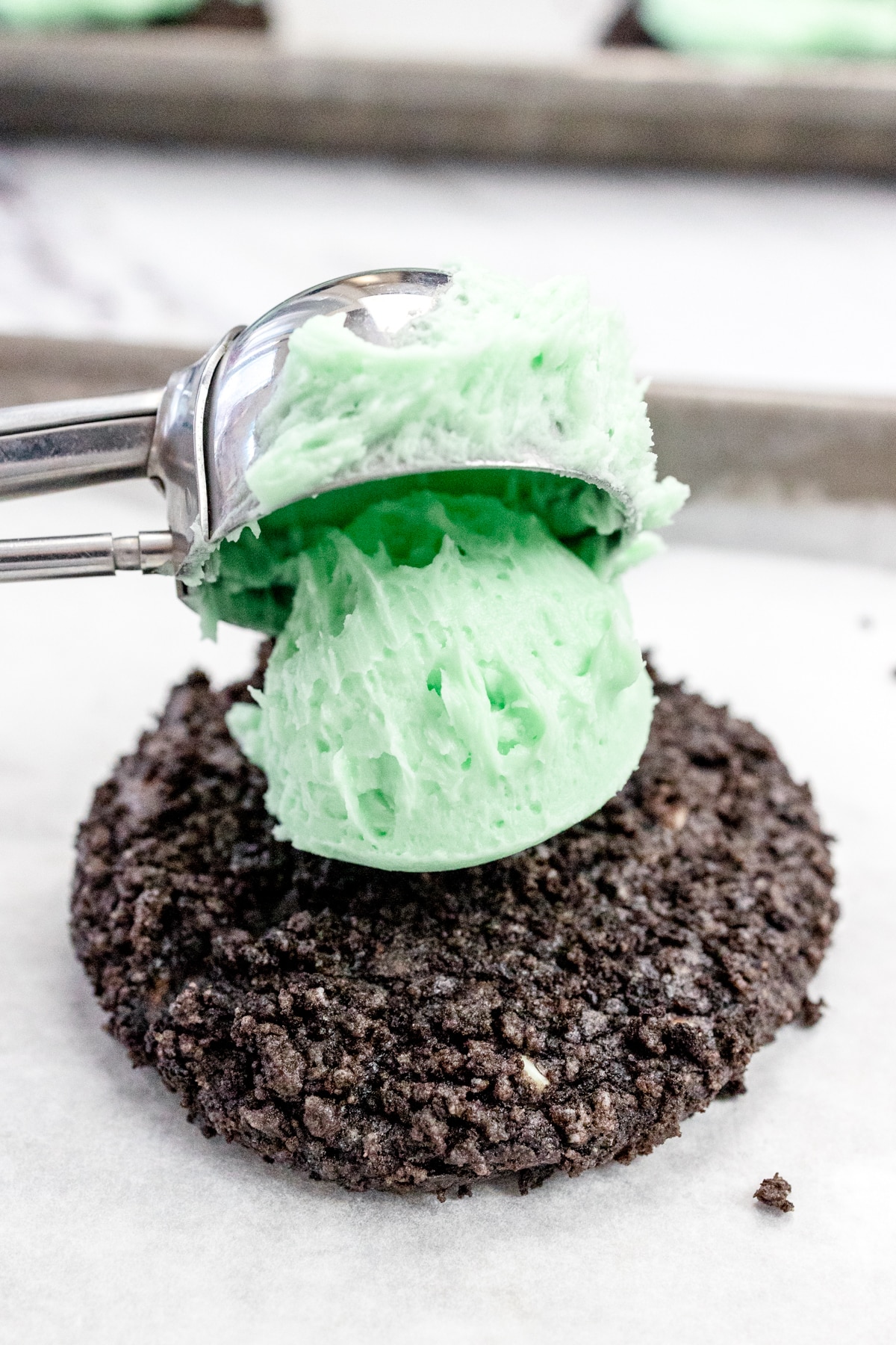 Close up of a cookie scoop placing a scoop of mint frosting onto a mint oreo cookie.