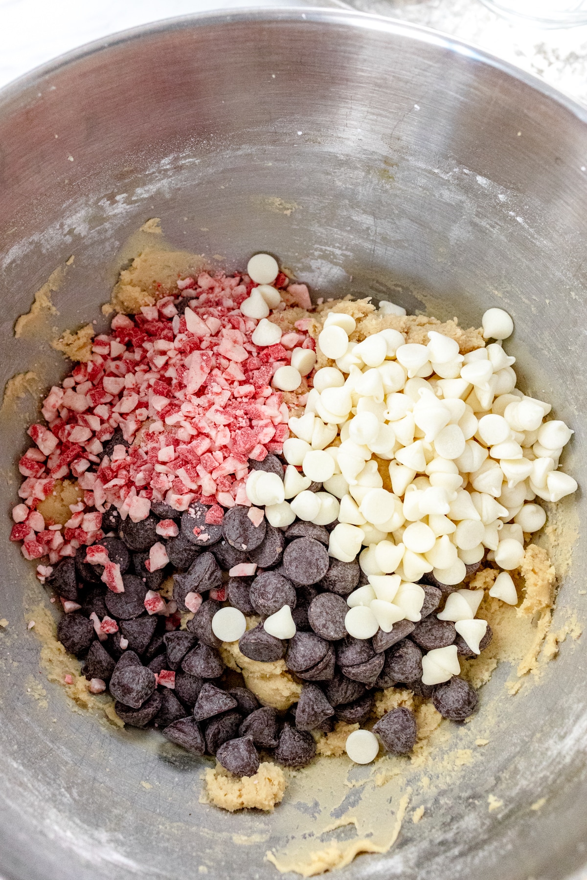 Close up of the bowl of a stand mixer with a creamed mixture in it with chocolate chips and peppermint pieces on top.