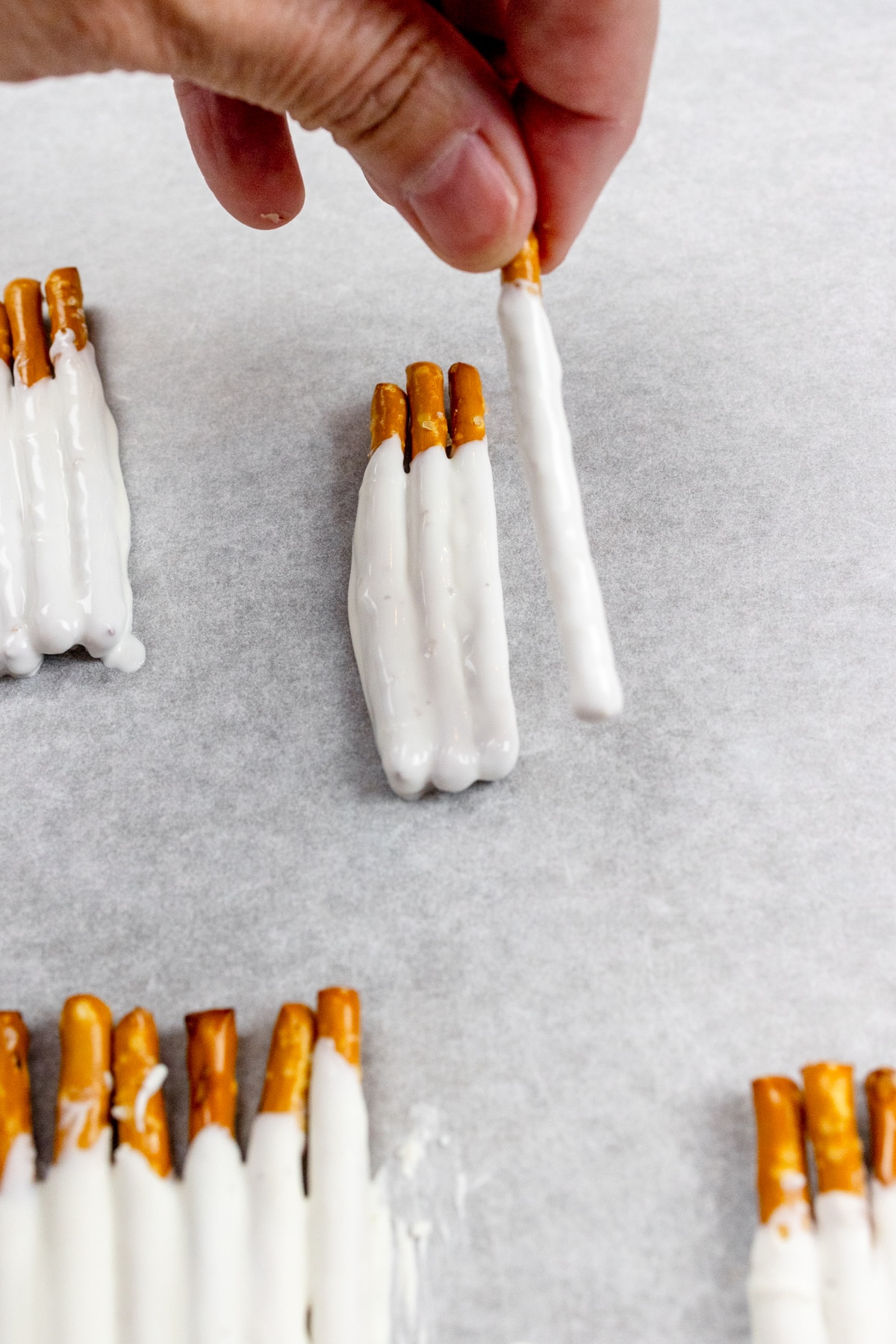 Close up of groups of 5-6 pretzel sticks individually dipped in white chocolate, on a baking tray lined with parchment paper.