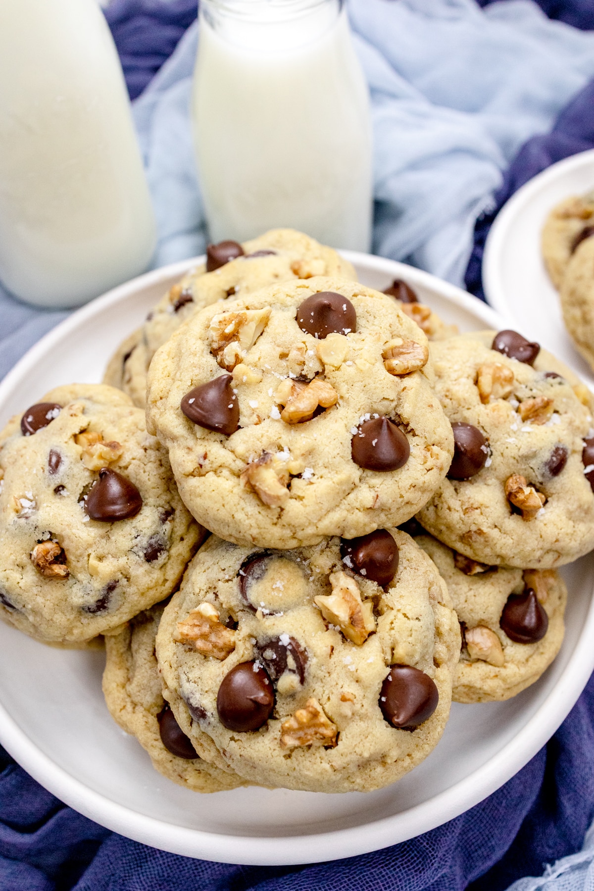 Close up view of Chocolate Chip Walnut Cookies on a white plate with glasses of milk beside it.