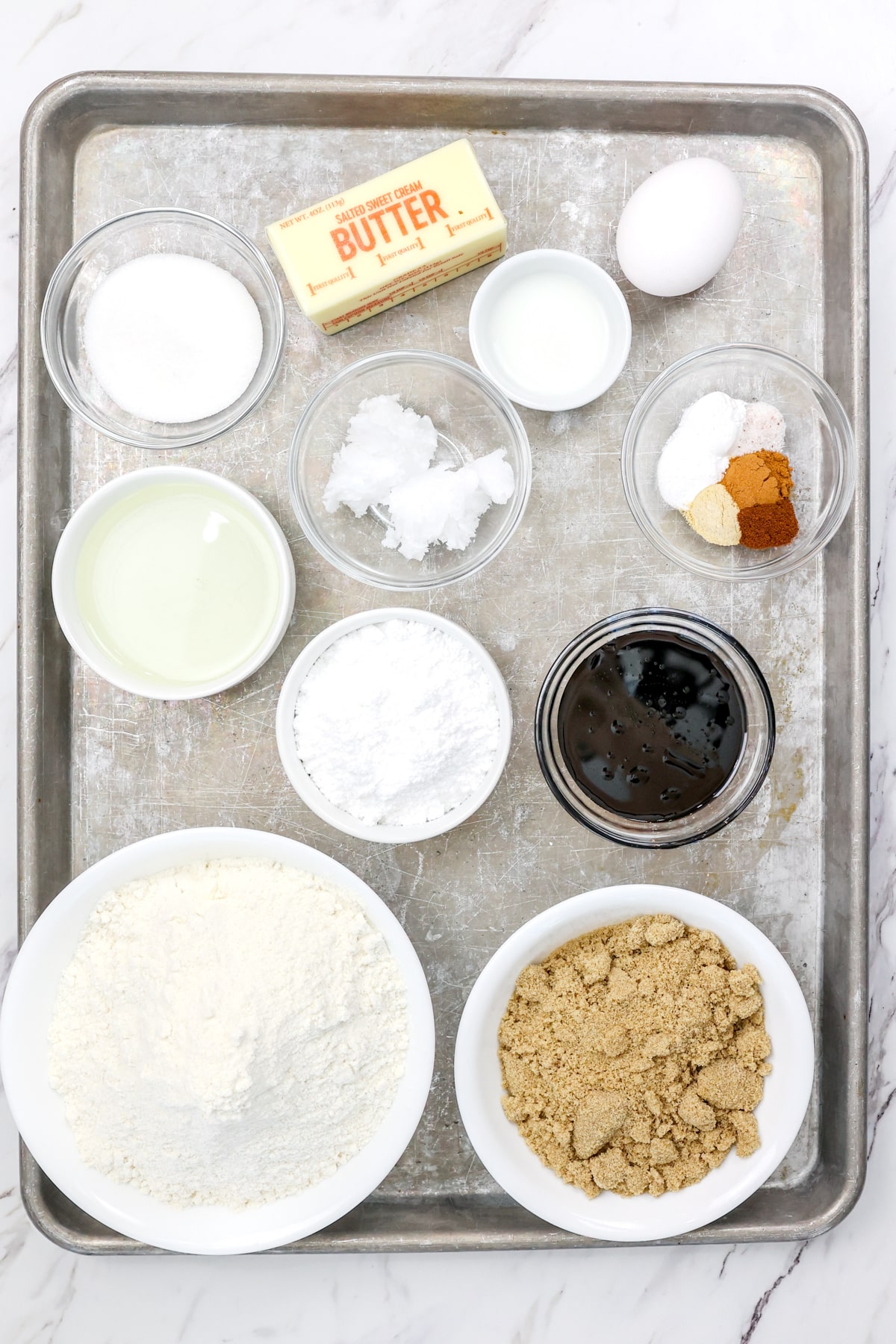 Top view of ingredients needed to make Gingerbread Sugar Cookies in small bowls on a baking tray.