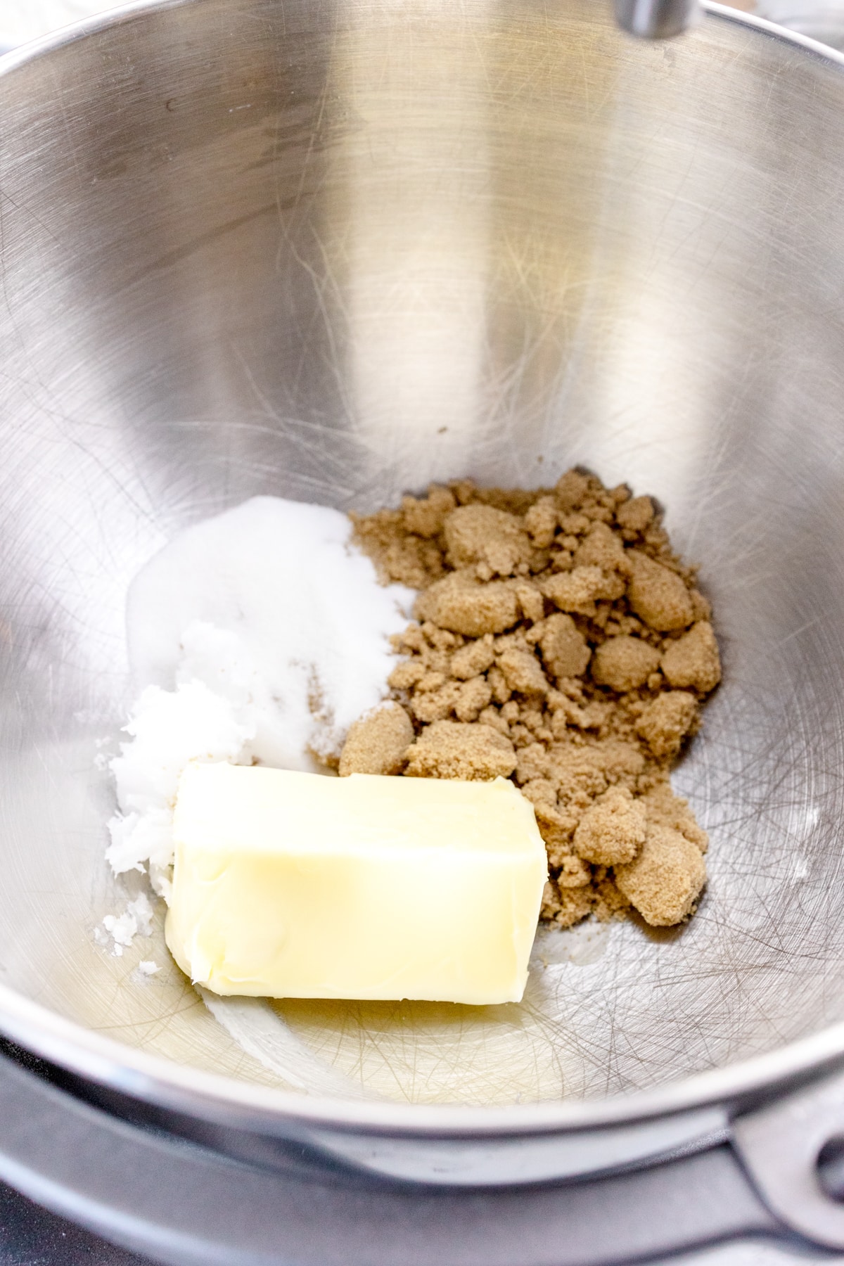Close up of the bowl of a stand mixer with butter, coconut oil, sugar, and brown sugar in it.