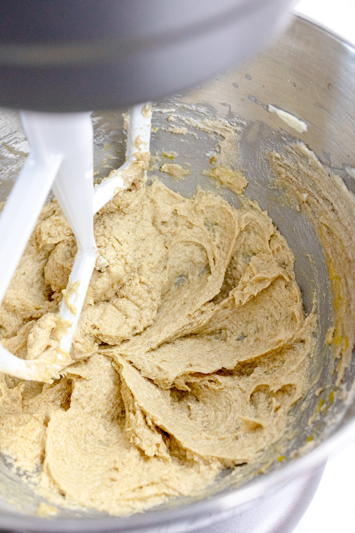Close up of the bowl of a stand mixer with butter mixture being mixed together with a paddle attachment.
