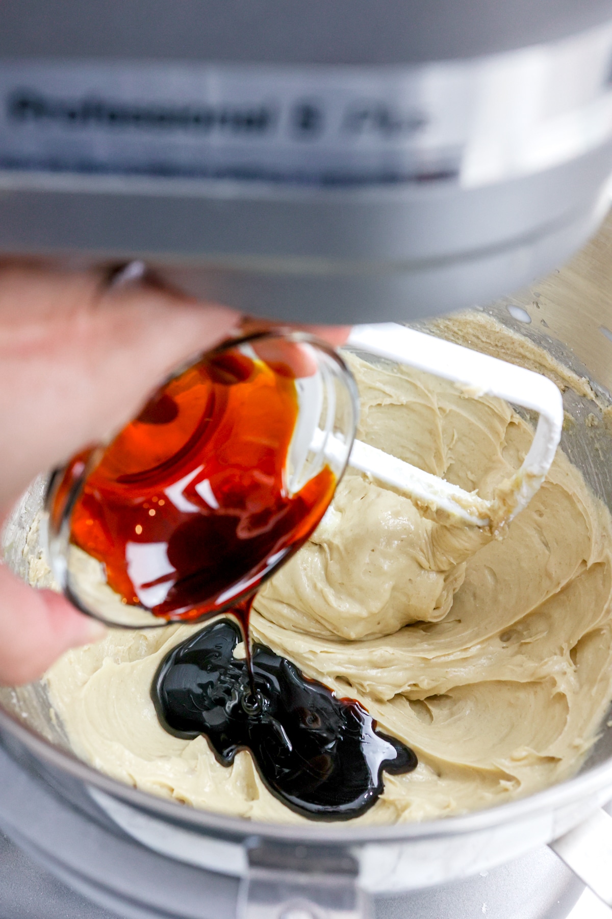 Close up of the bowl of a stand mixer with molasses being added to the creamed mixture.