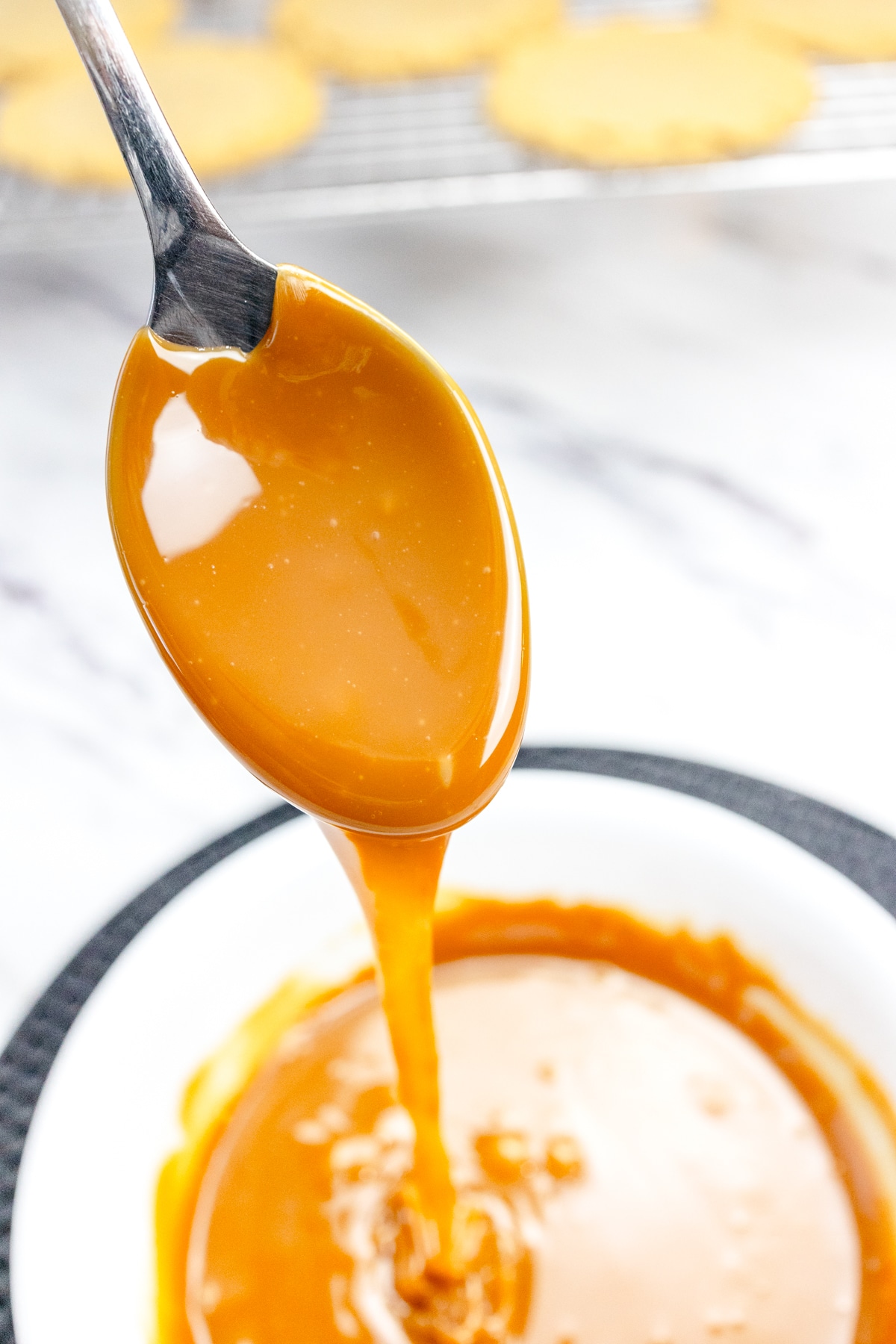 Close up of a spoon being lifted out of a small bowl filled with the caramel topping mixture.