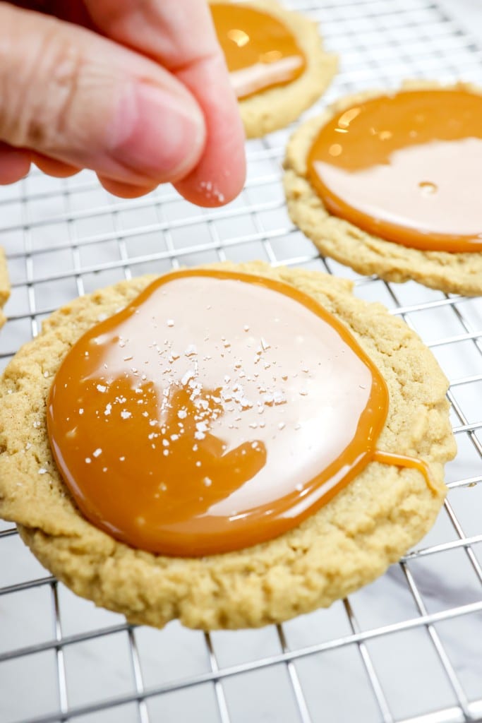 Close up of salt being sprinkled onto the caramel topping on a cookie on a wire rack.