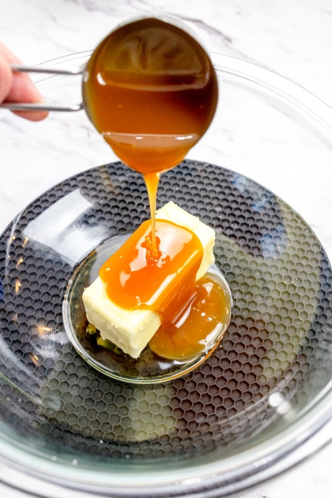 Close up of caramel syrup being poured over a stick of butter in a glass bowl.