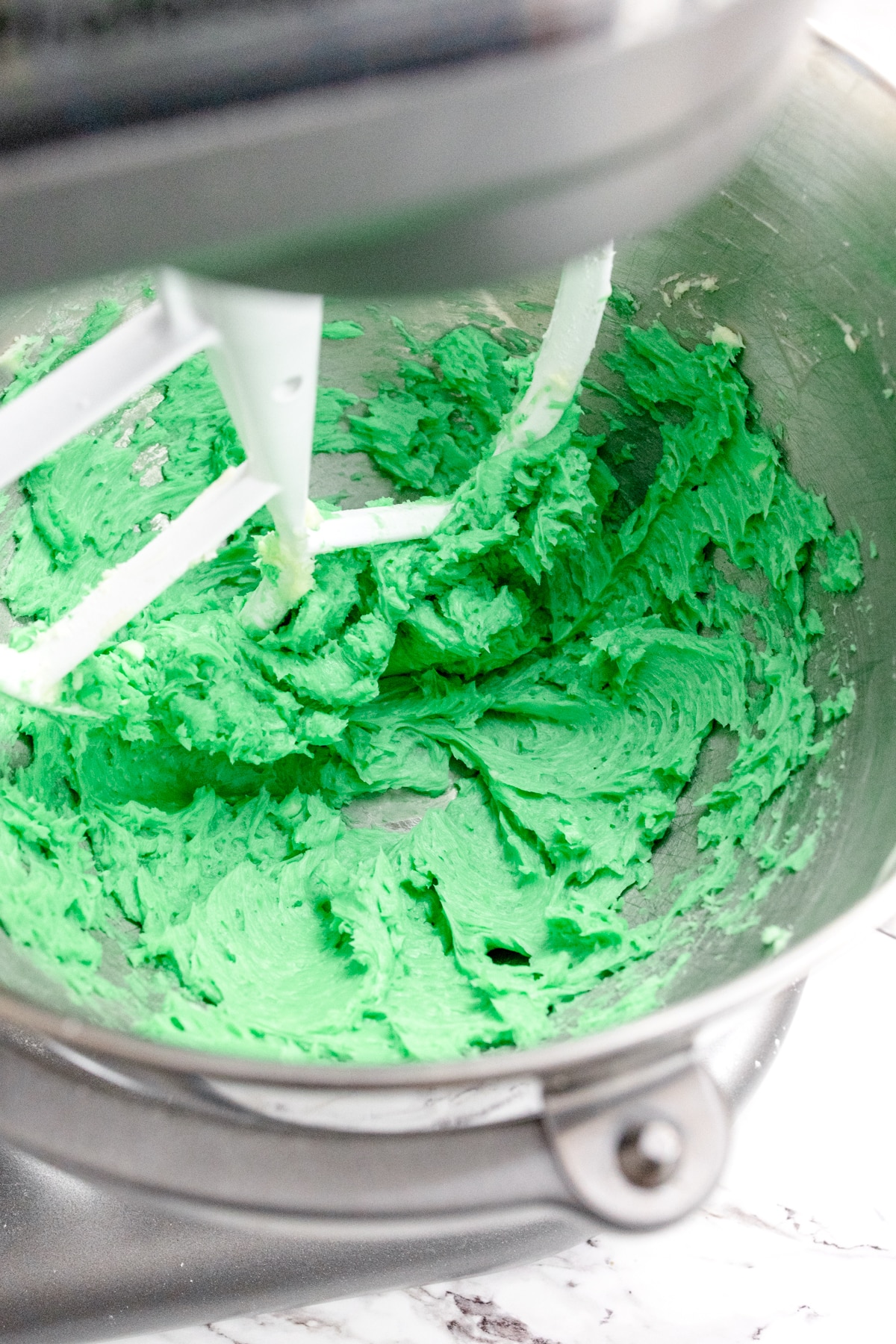 Close up of the bowl of a stand mixer with a creamed mixture in it that has been colored green.