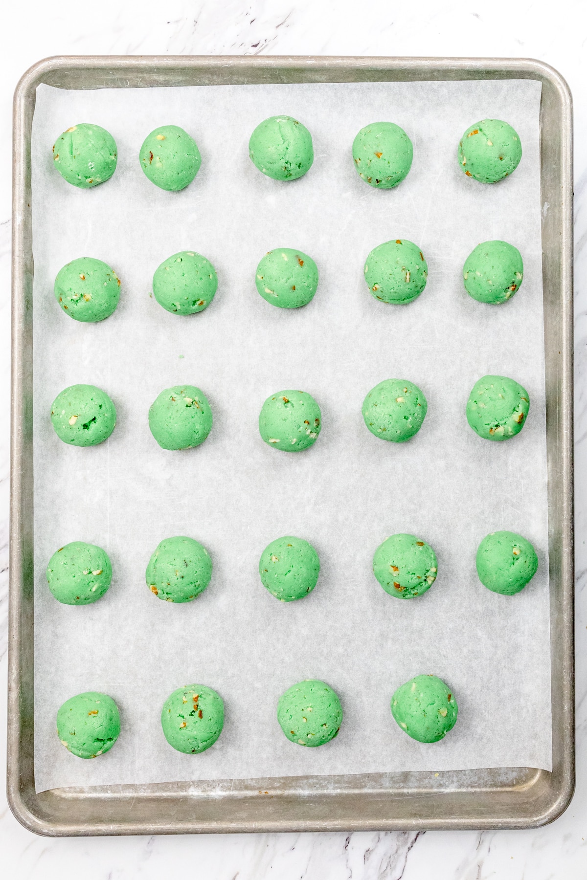 Top view of baking tray lined with parchment paper with Cookie dough balls on it.