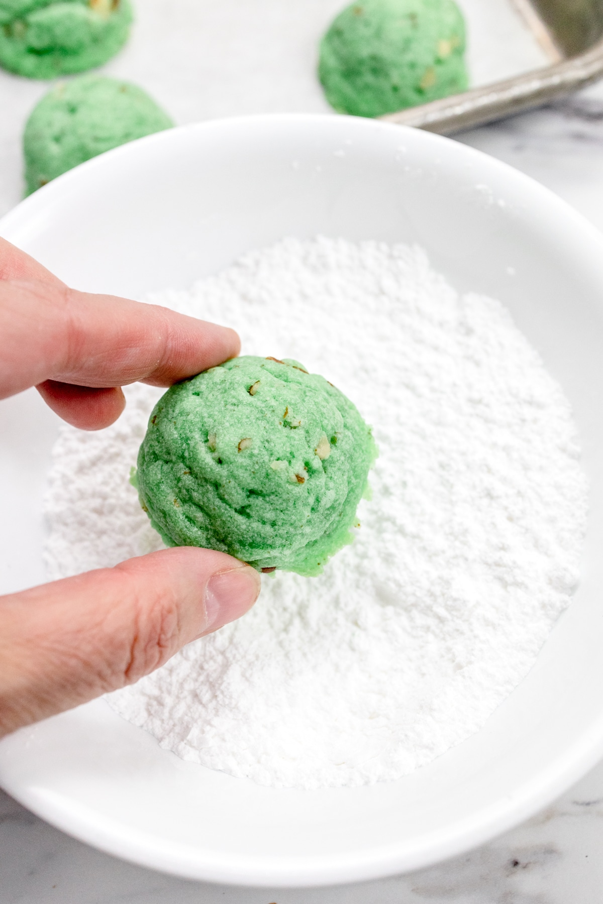 Close up view of a hand placing a cookie into a bowl of powdered sugar.