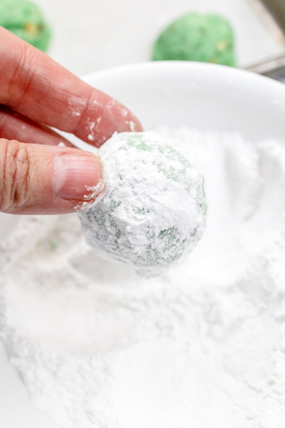 Close up view of a hand rolling a cookie in a bowl of powdered sugar.