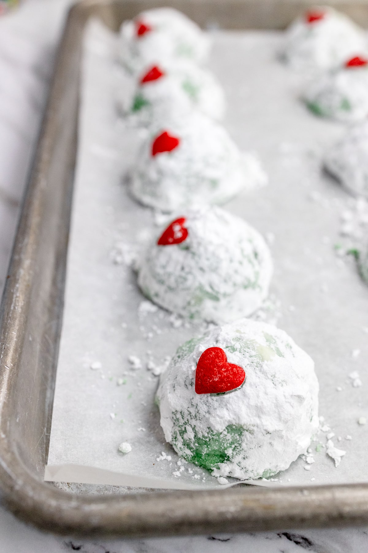 Close up view of finished Grinch Snowball Cookies on a baking tray lined with parchment paper.