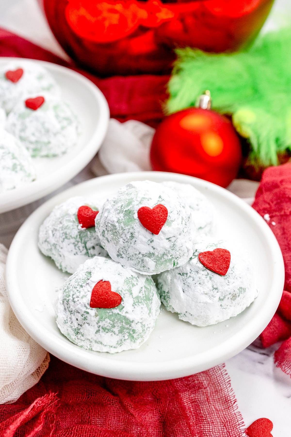 Close up of Grinch Snowball Cookies on a white plate, with Christmas decorations around them.