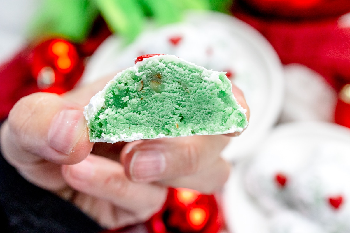 Close up of someone holding up a Grinch Snowball Cookie in their hand, that's been sliced in half to reveal the middle