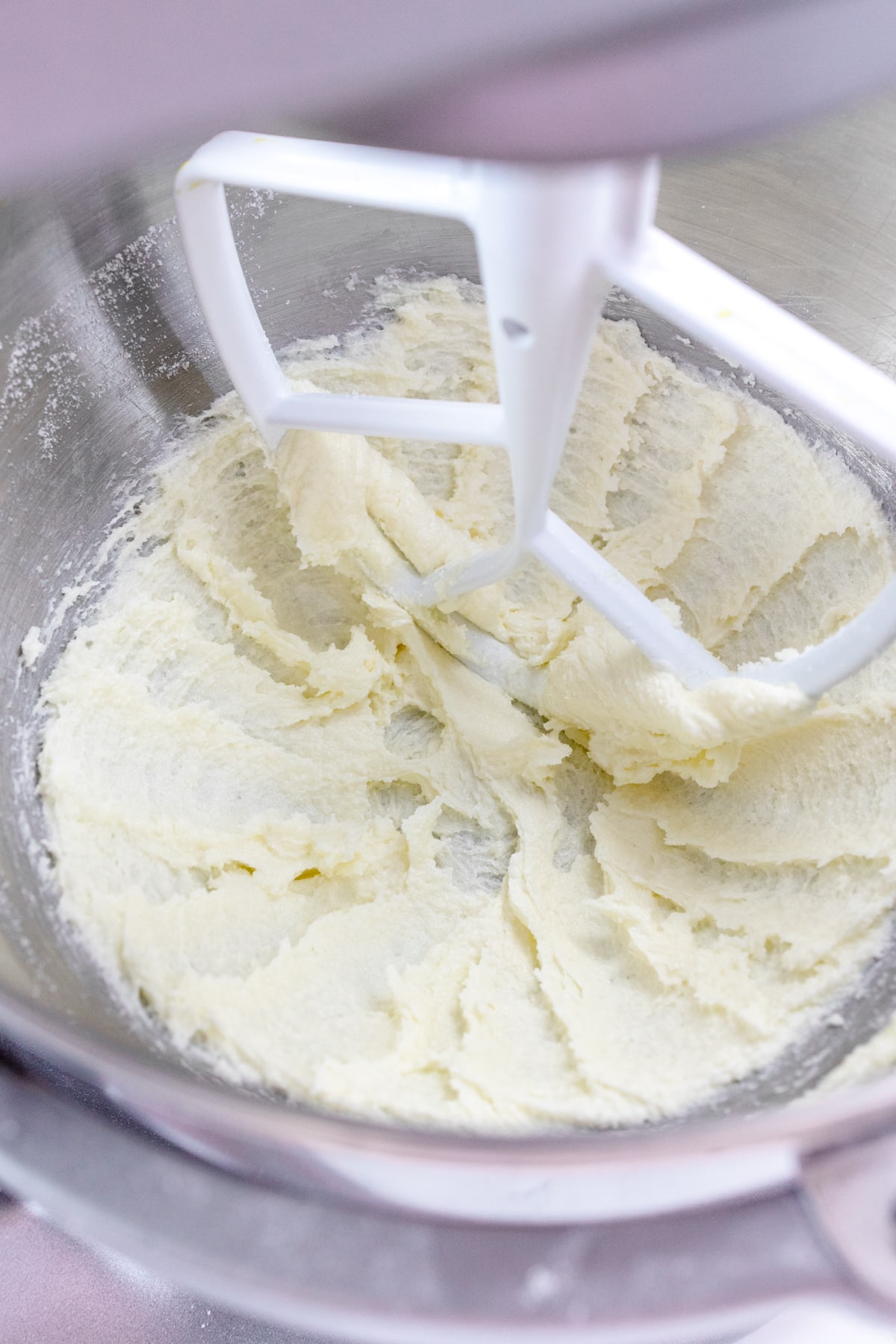 Close up of the bowl of a stand mixer with butter and sugar being creamed together with a paddle attachment.