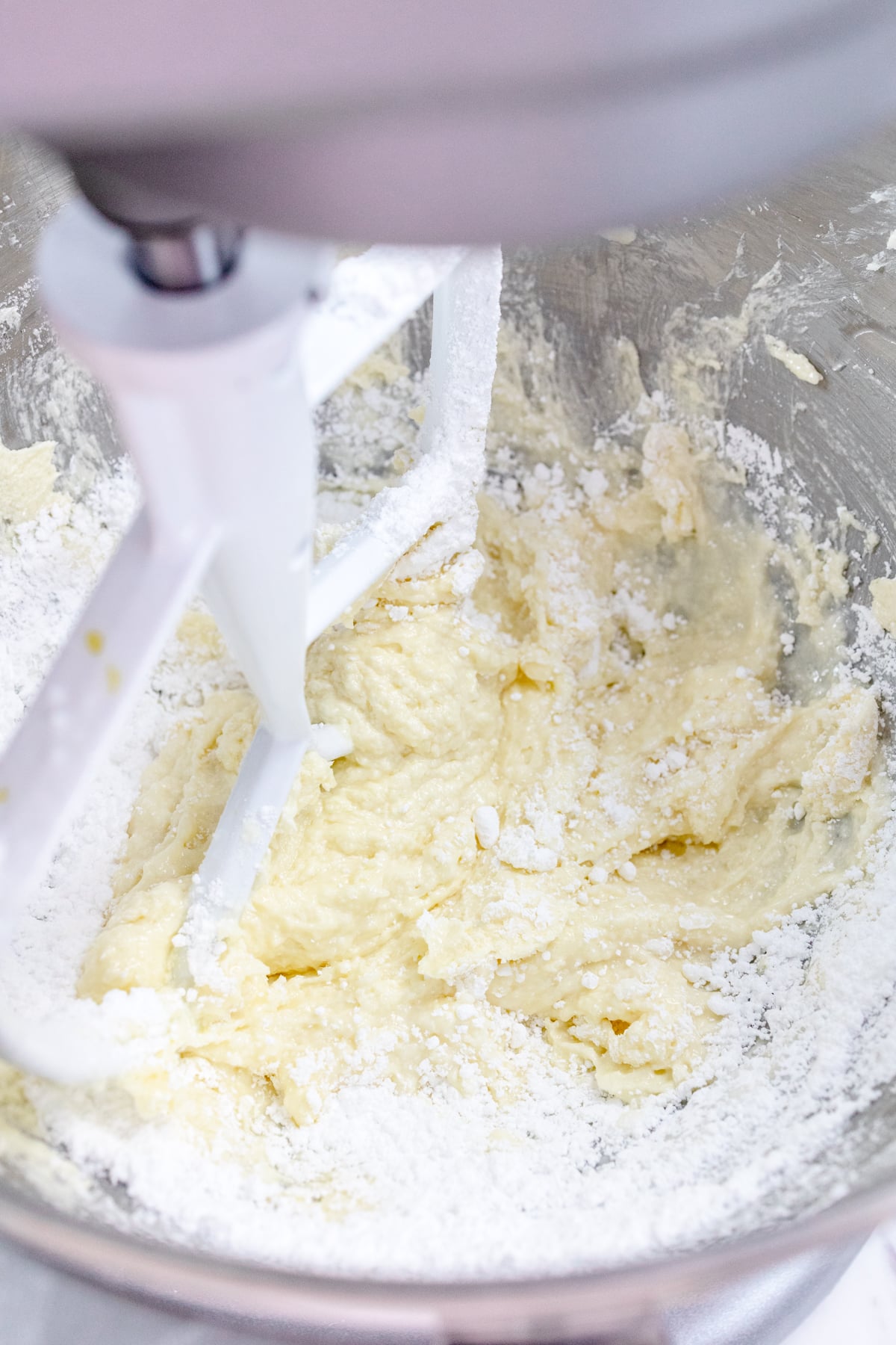 Close up of the bowl of a stand mixer with dry and wet ingredients being mixed together with a paddle attachment.