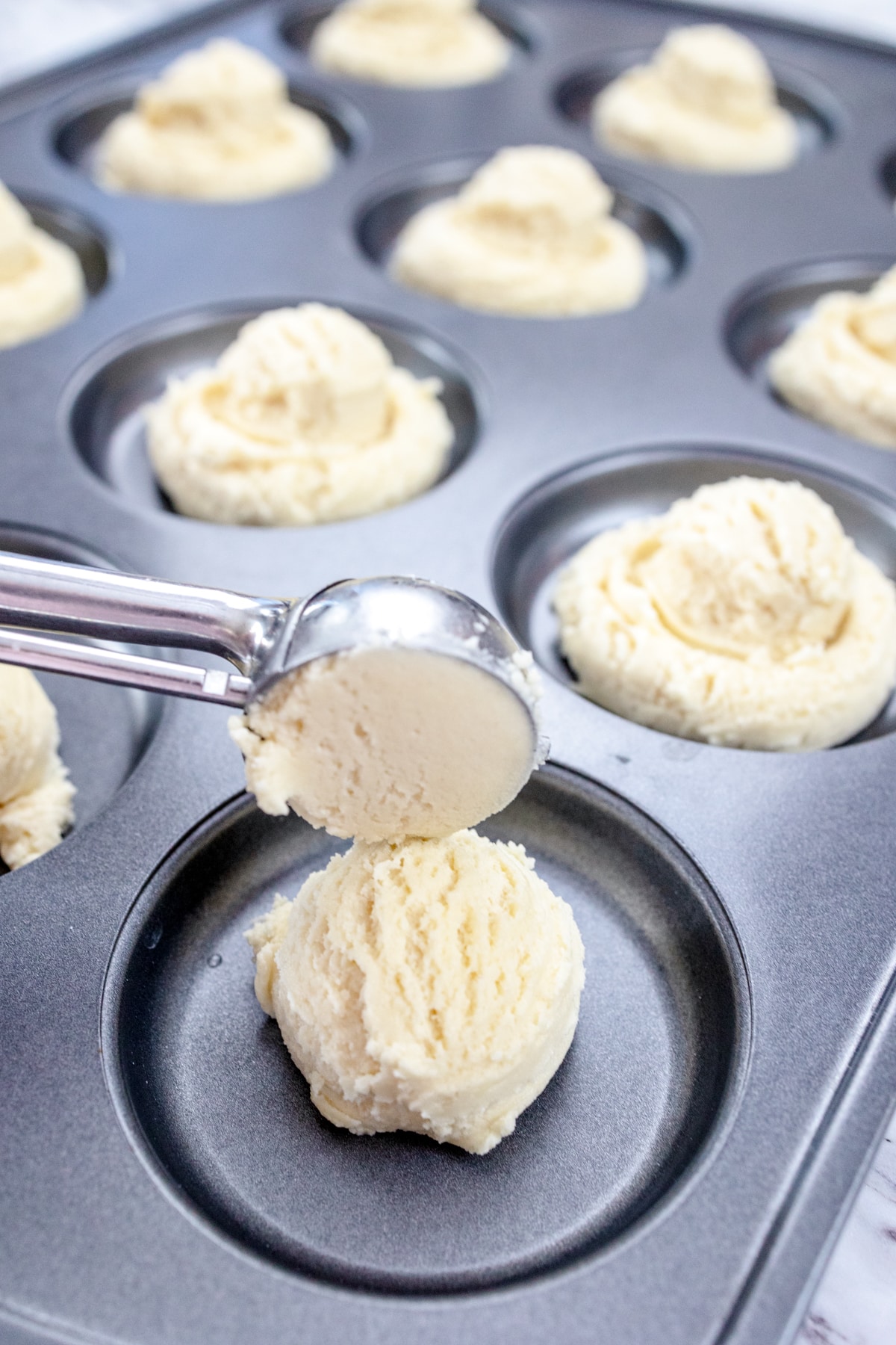Close up of a cookie scoop placing a scoop of cookie dough into the well of a muffin top pan.