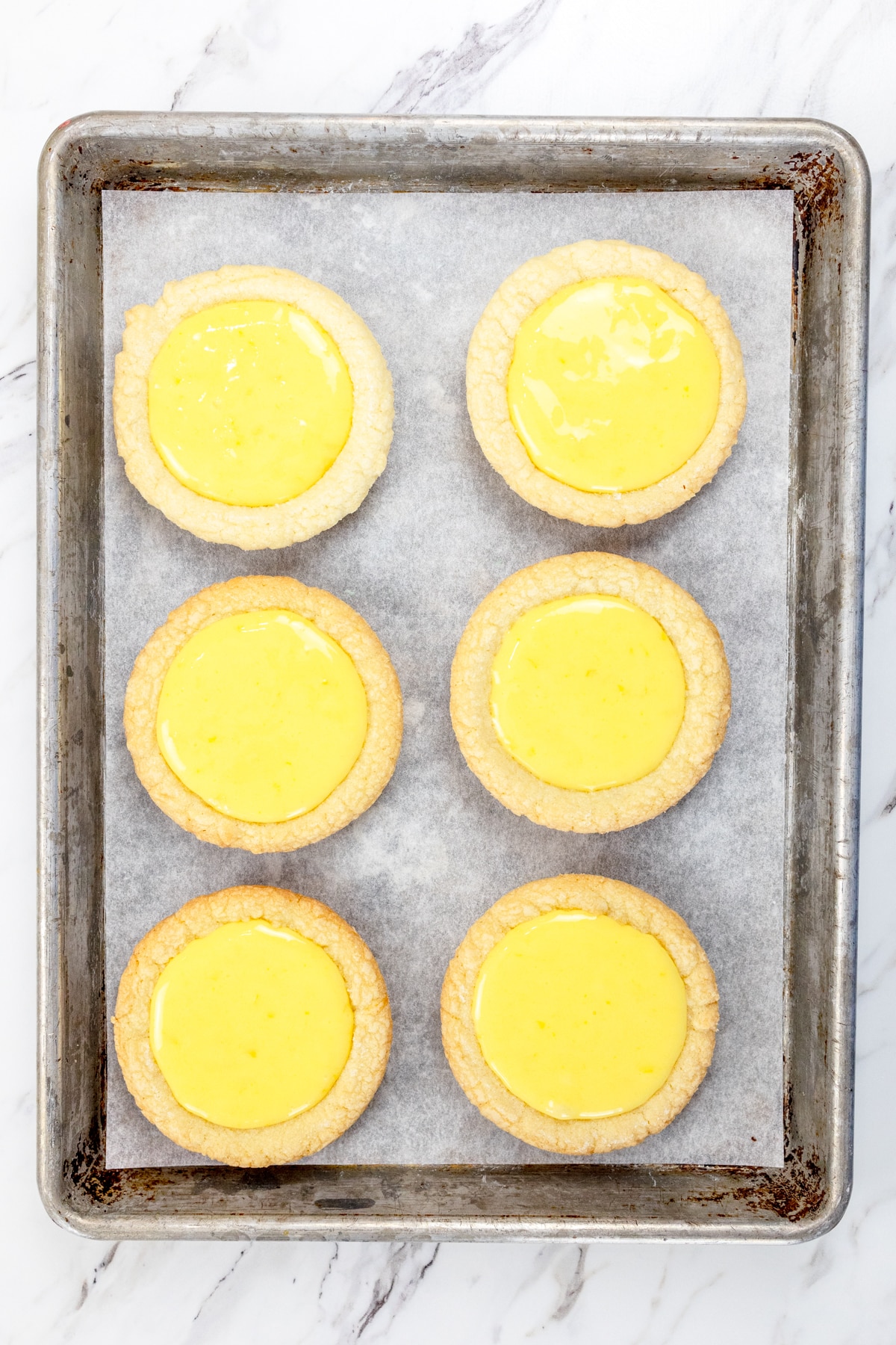 Top view of cookies filled with lemon curd filling on a baking tray lined with parchment paper.