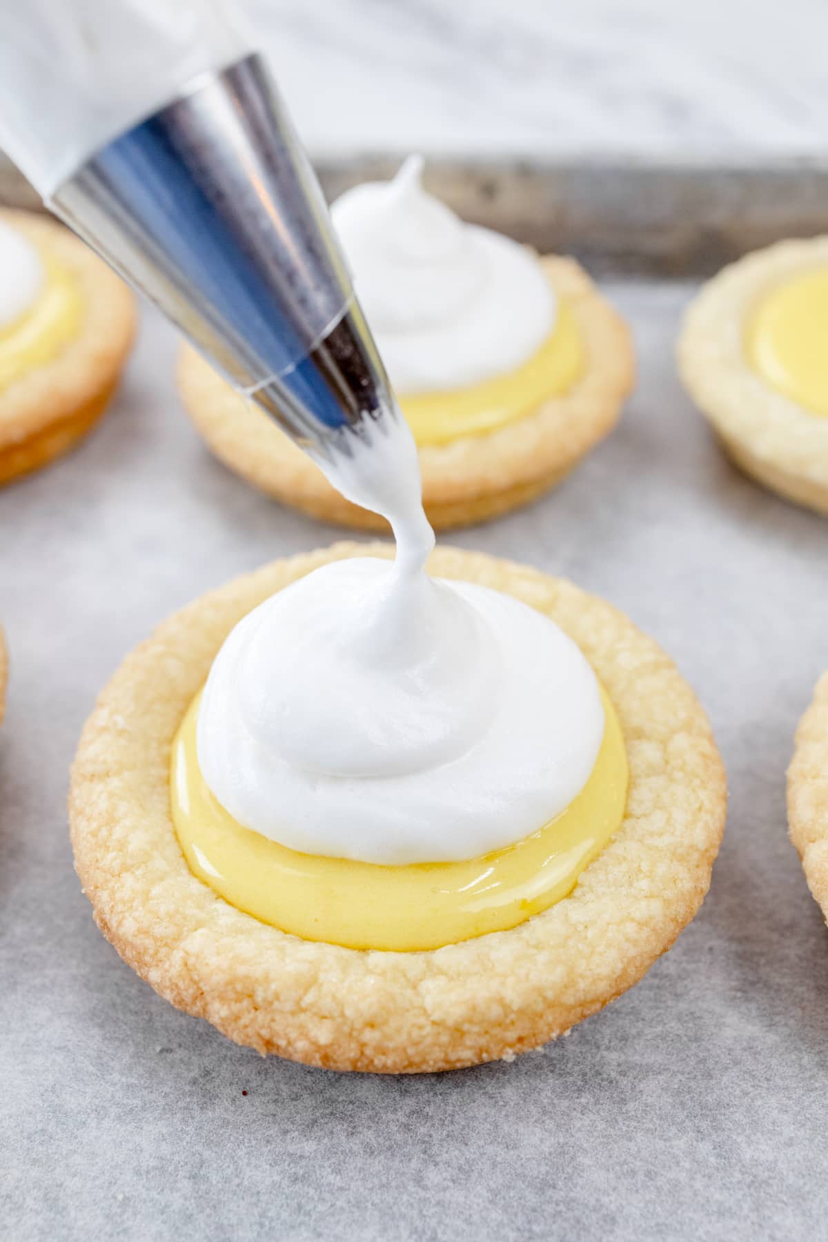 Close up view of meringue topping being piped onto lemon-filled cookies.