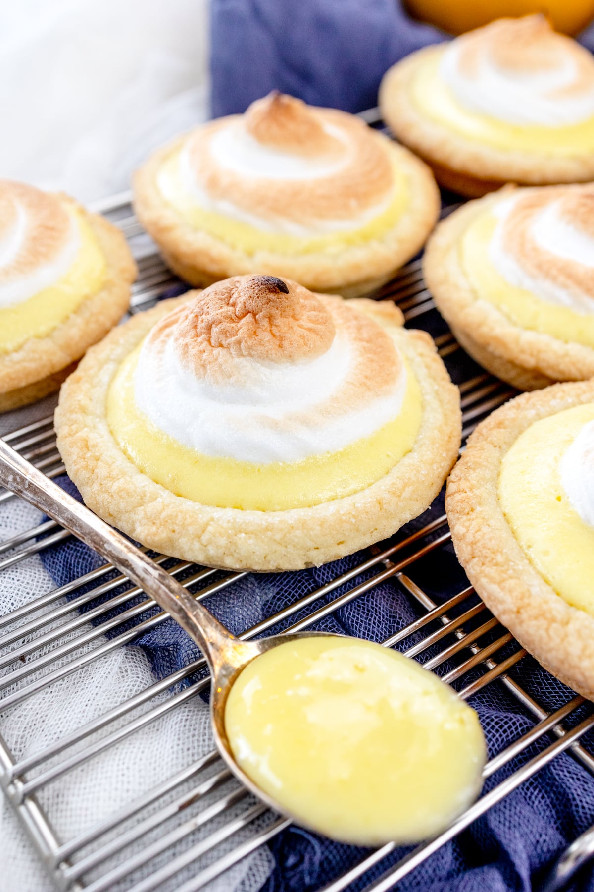 Close up view of Lemon Meringue Cookies on a wire rack, with a spoon filled with lemon curd next to them.