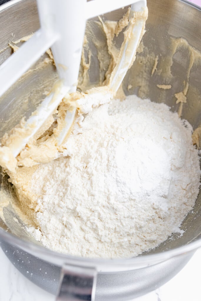 Close up of the bowl of a stand mixer with a creamed mixture in the bottom and a flour mixture on top.